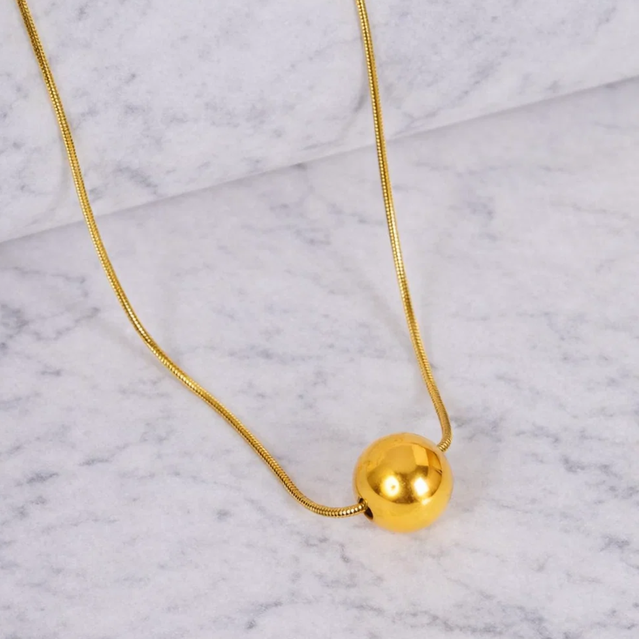 Gold necklace with a spherical pendant on a marble surface