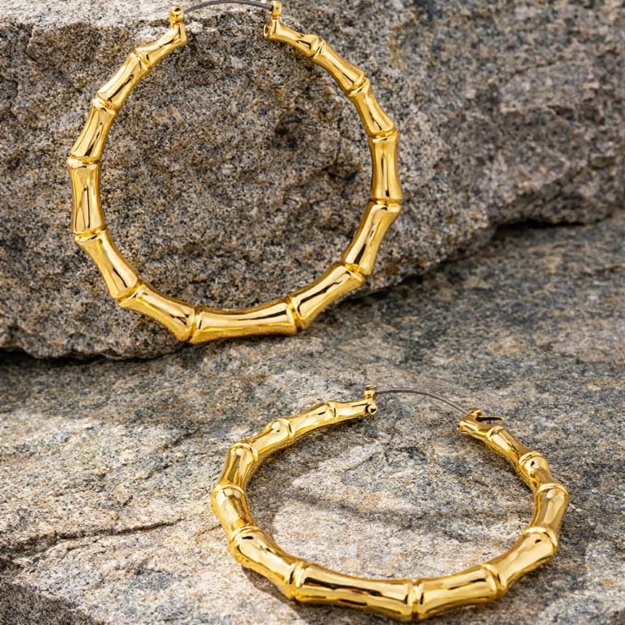 Gold bamboo hoop earrings on a stone surface
