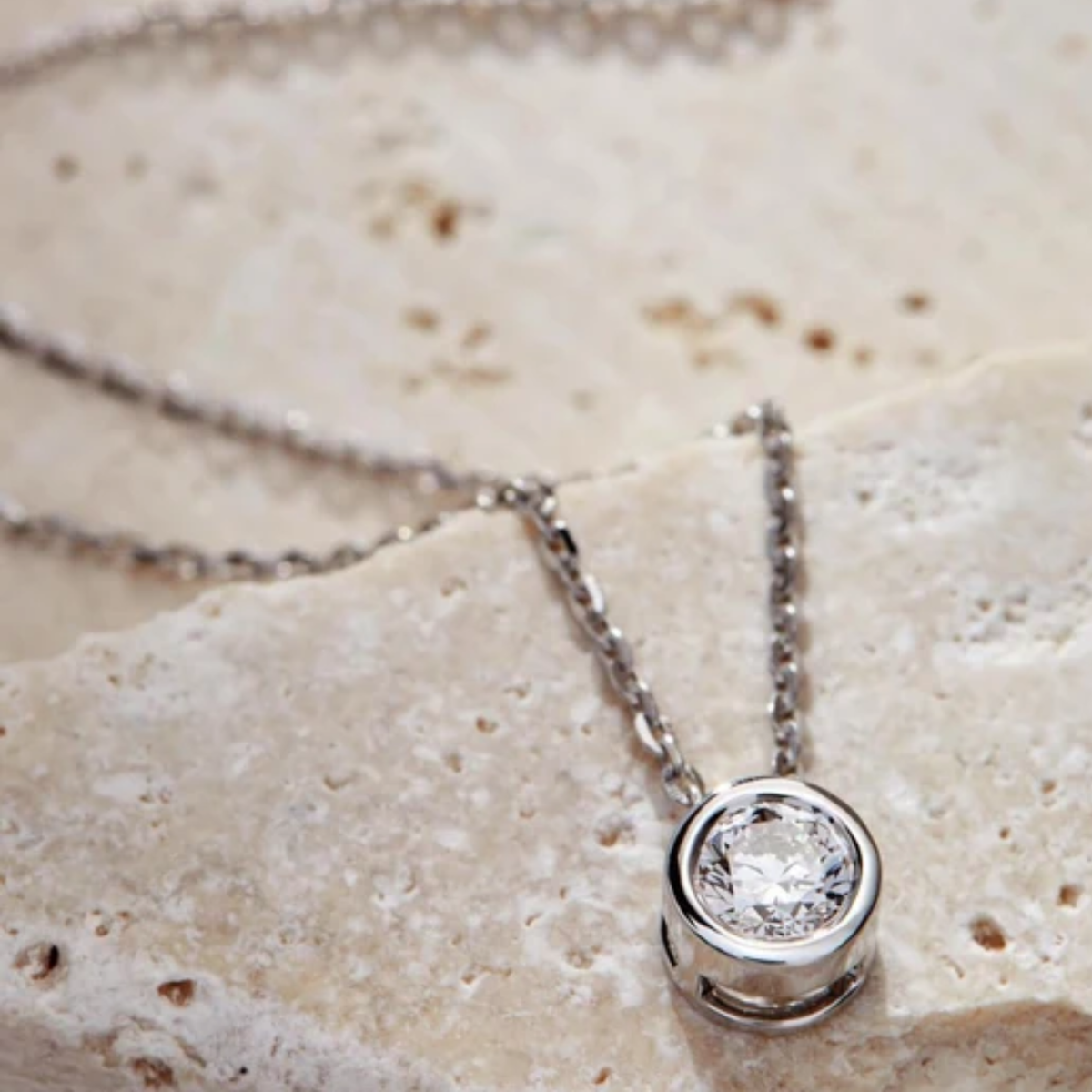 A silver necklace on a textured beige stone surface.