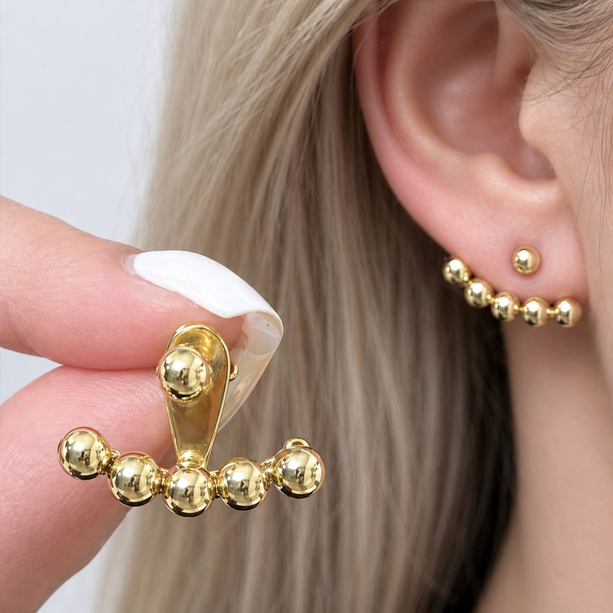 Gold earring being held near an ear with another gold earring on the ear.