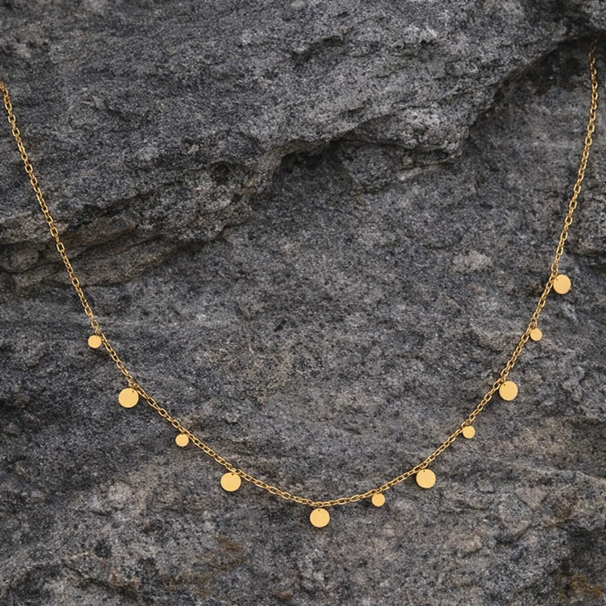 Gold necklace with small round pendants on a textured stone surface