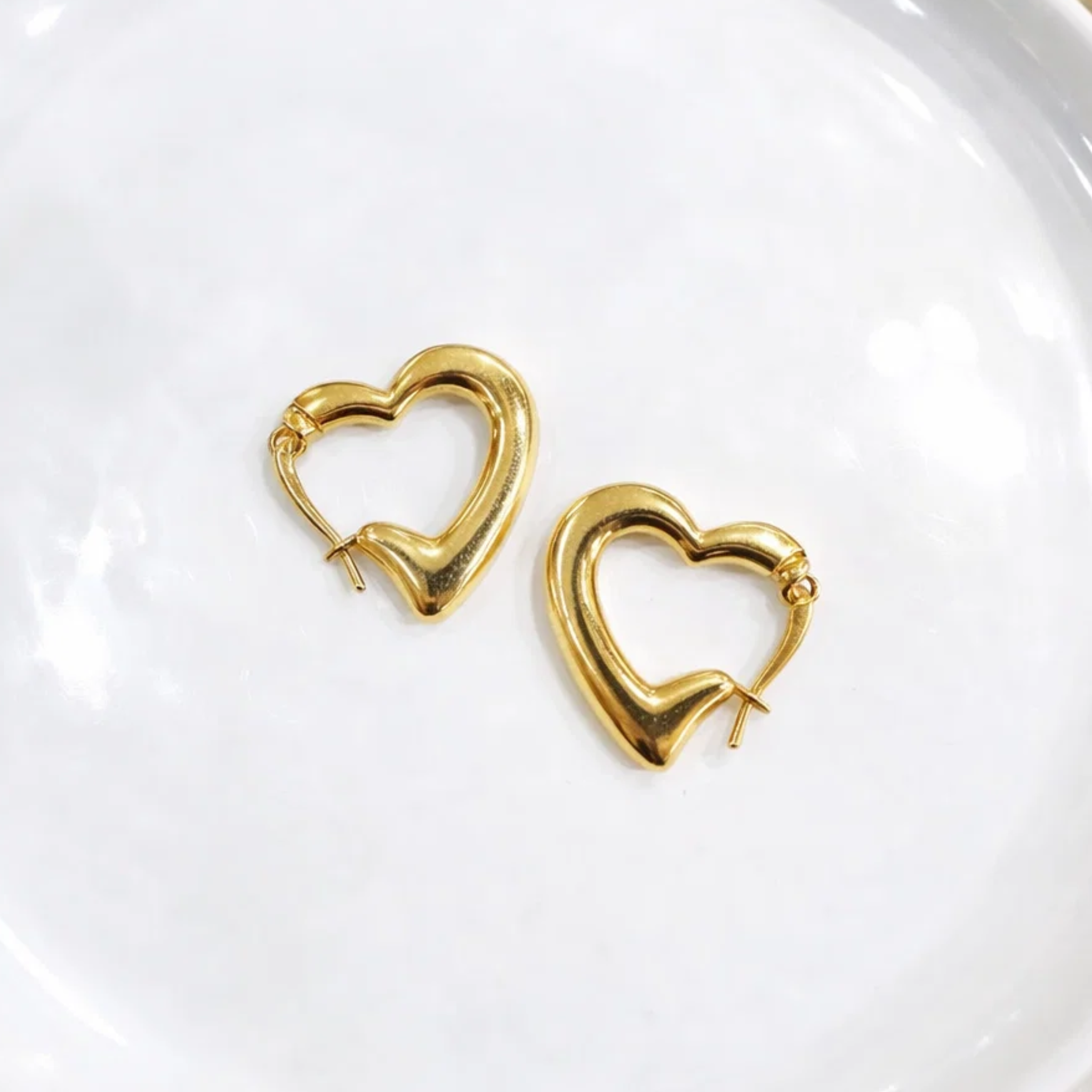 Gold heart-shaped hoop earrings on a white plate