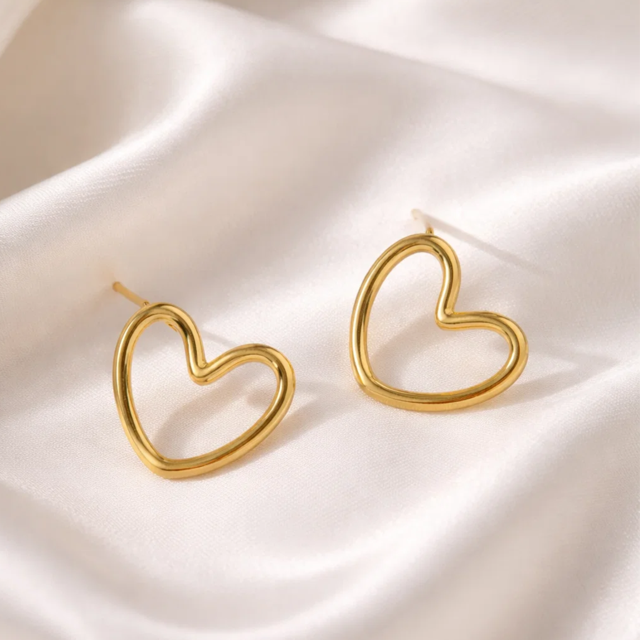 Gold heart-shaped earrings on a satin surface