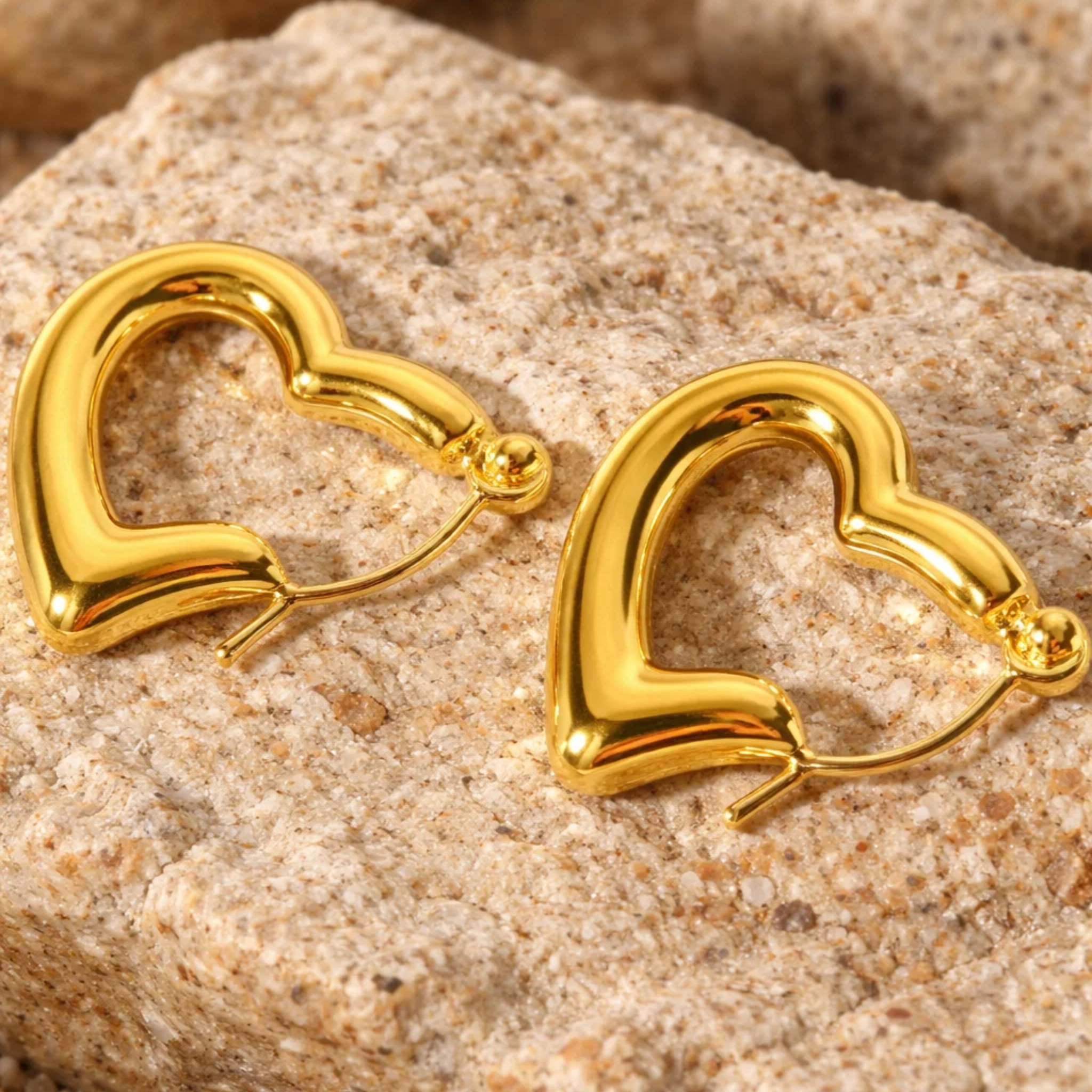 Gold heart-shaped earrings on a textured stone surface
