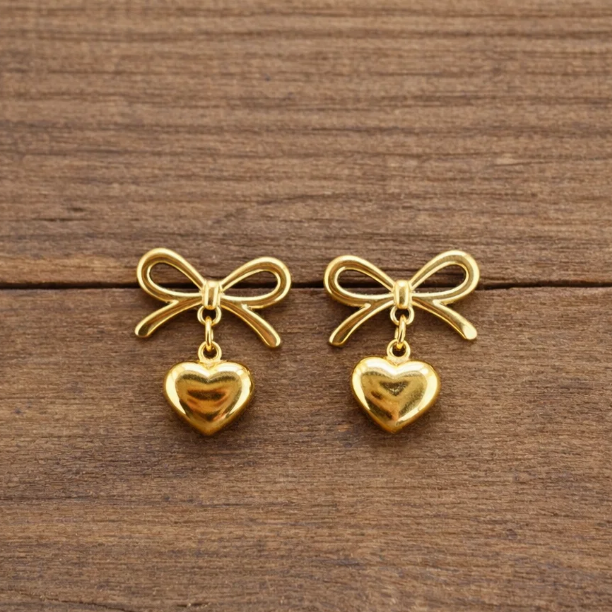Gold bow and heart earrings on a wooden surface