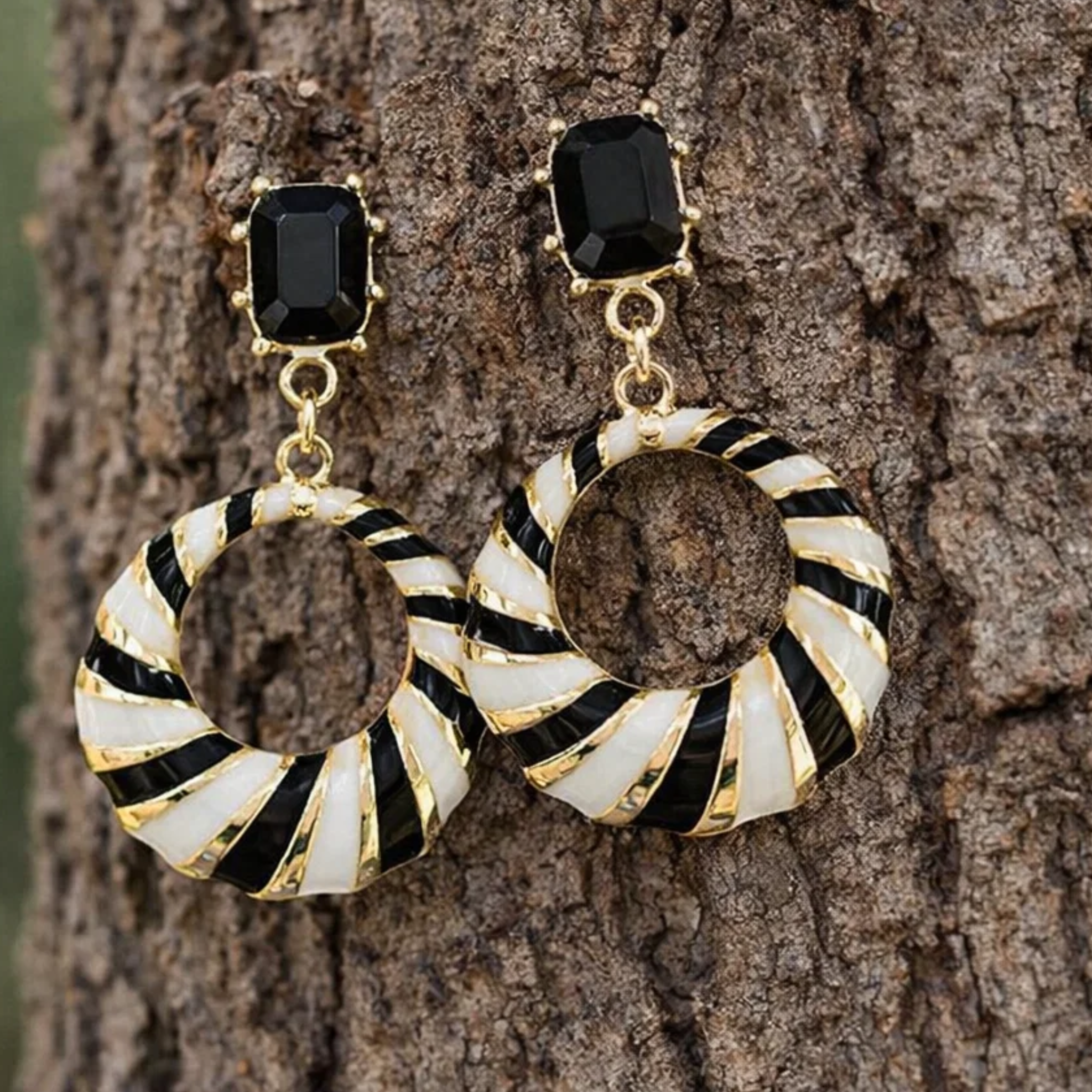 Gold and black earrings with circular design on a tree bark background