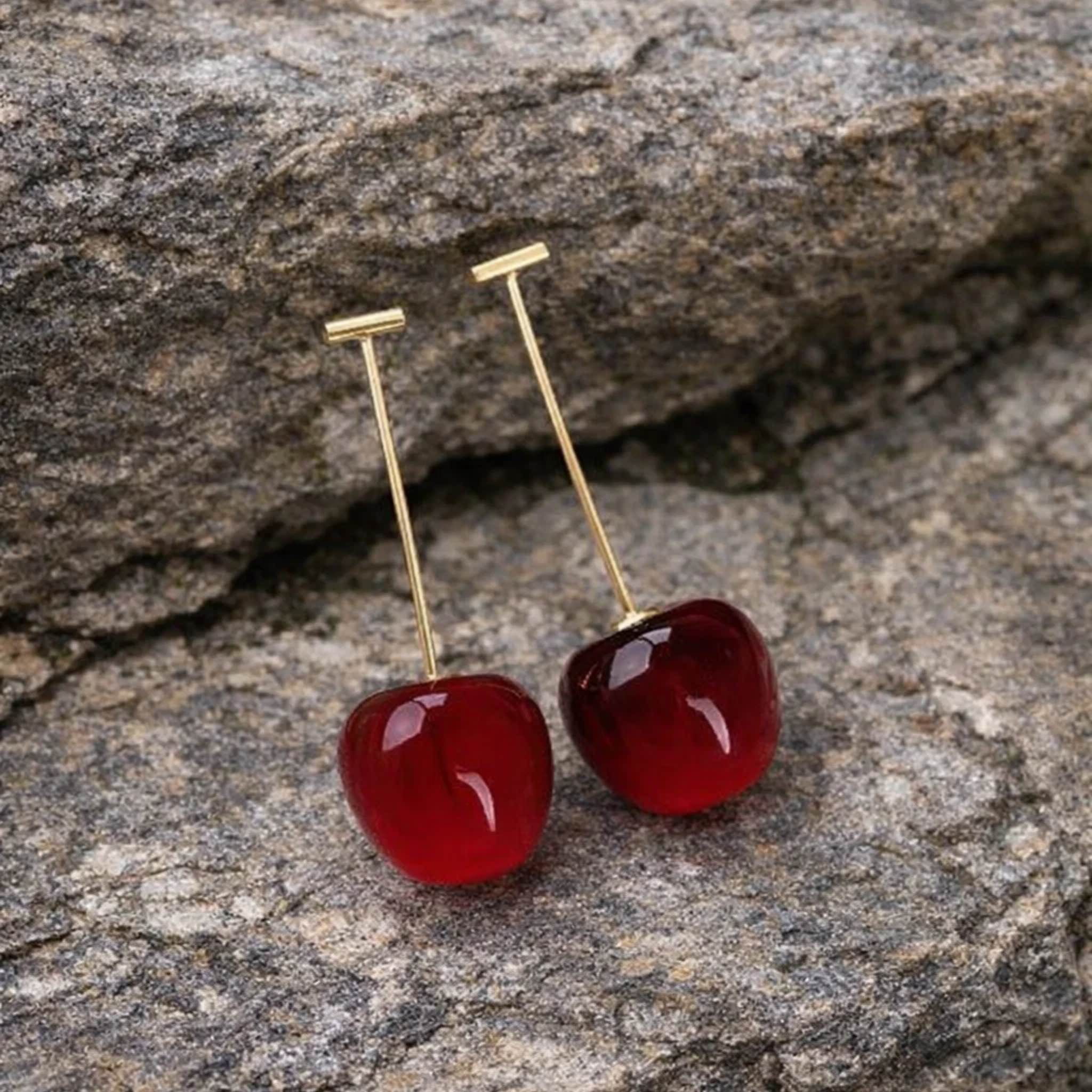 Red cherry-shaped earrings on a stone surface