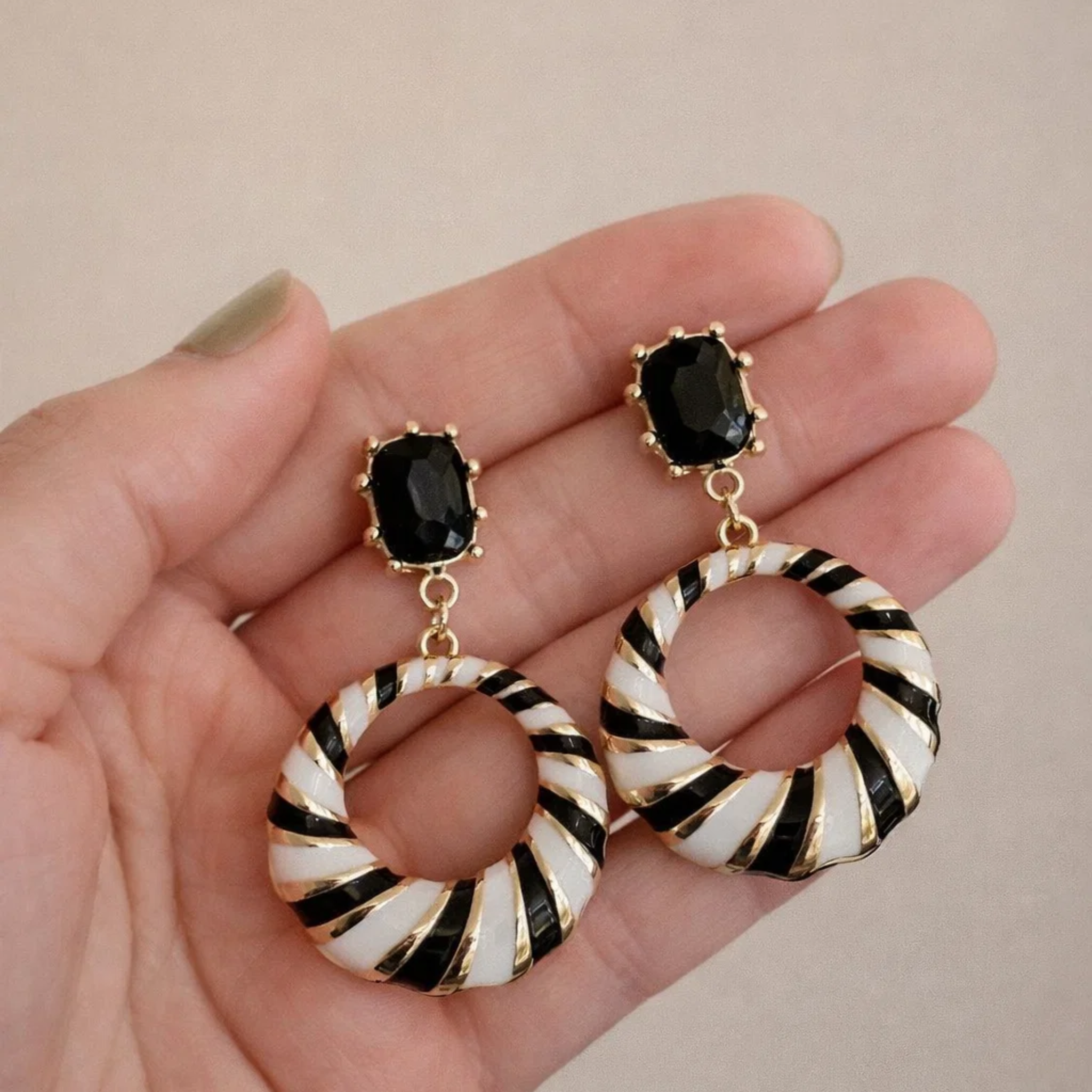 Earrings with black and gold design held in a hand 