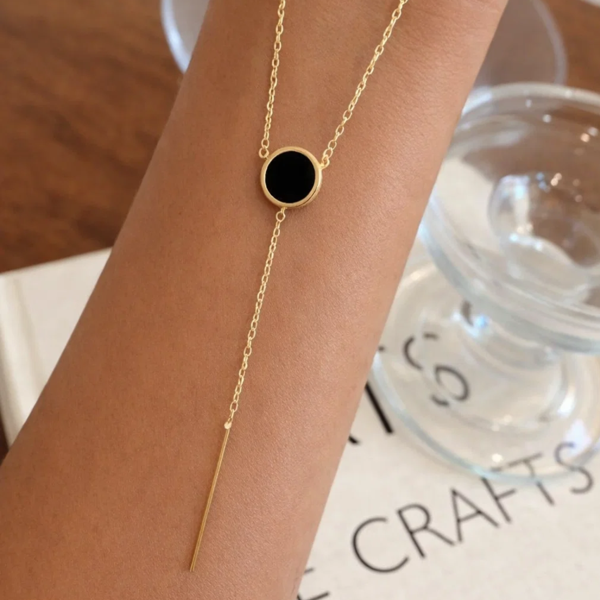 Gold necklace with a black pendant on a wrist