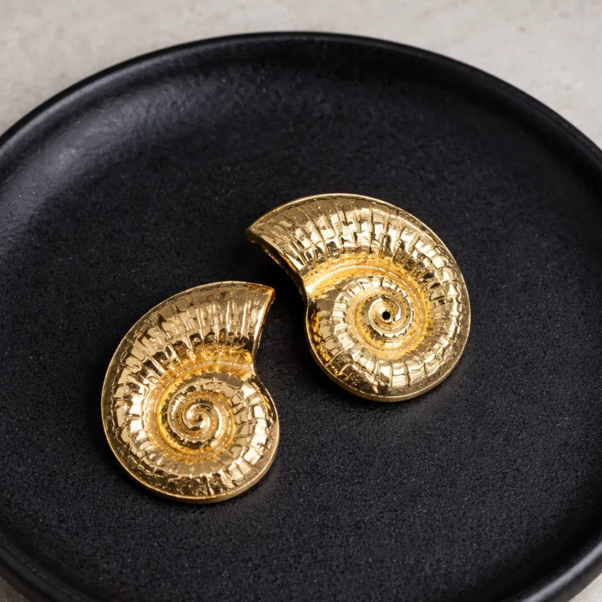 Gold spiral earrings on a black plate