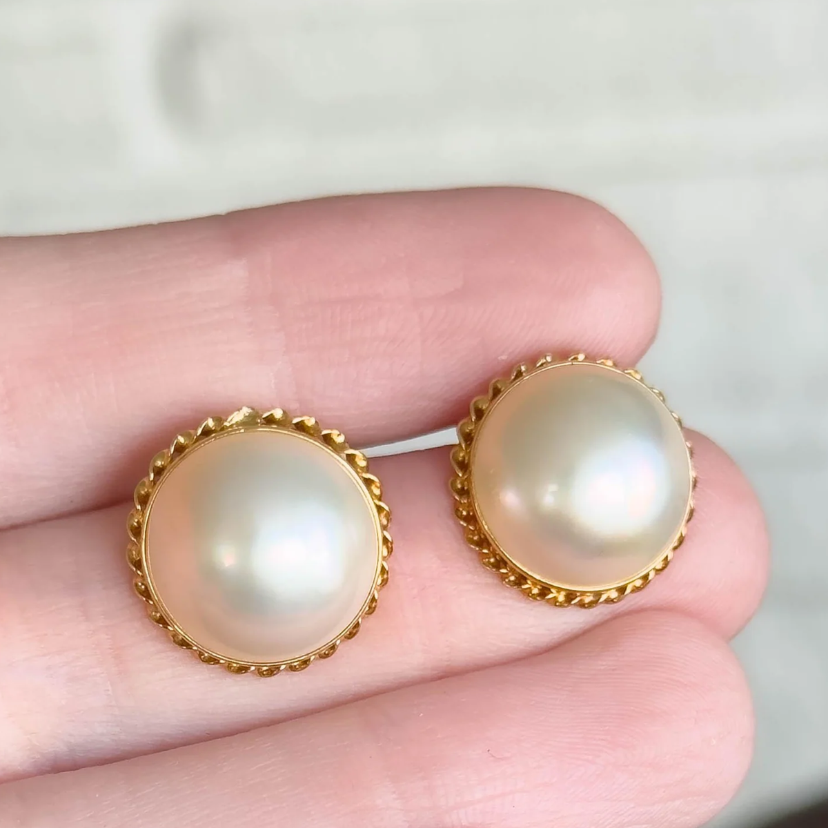 A pair of round pearl stud earrings with gold-toned scalloped bezels