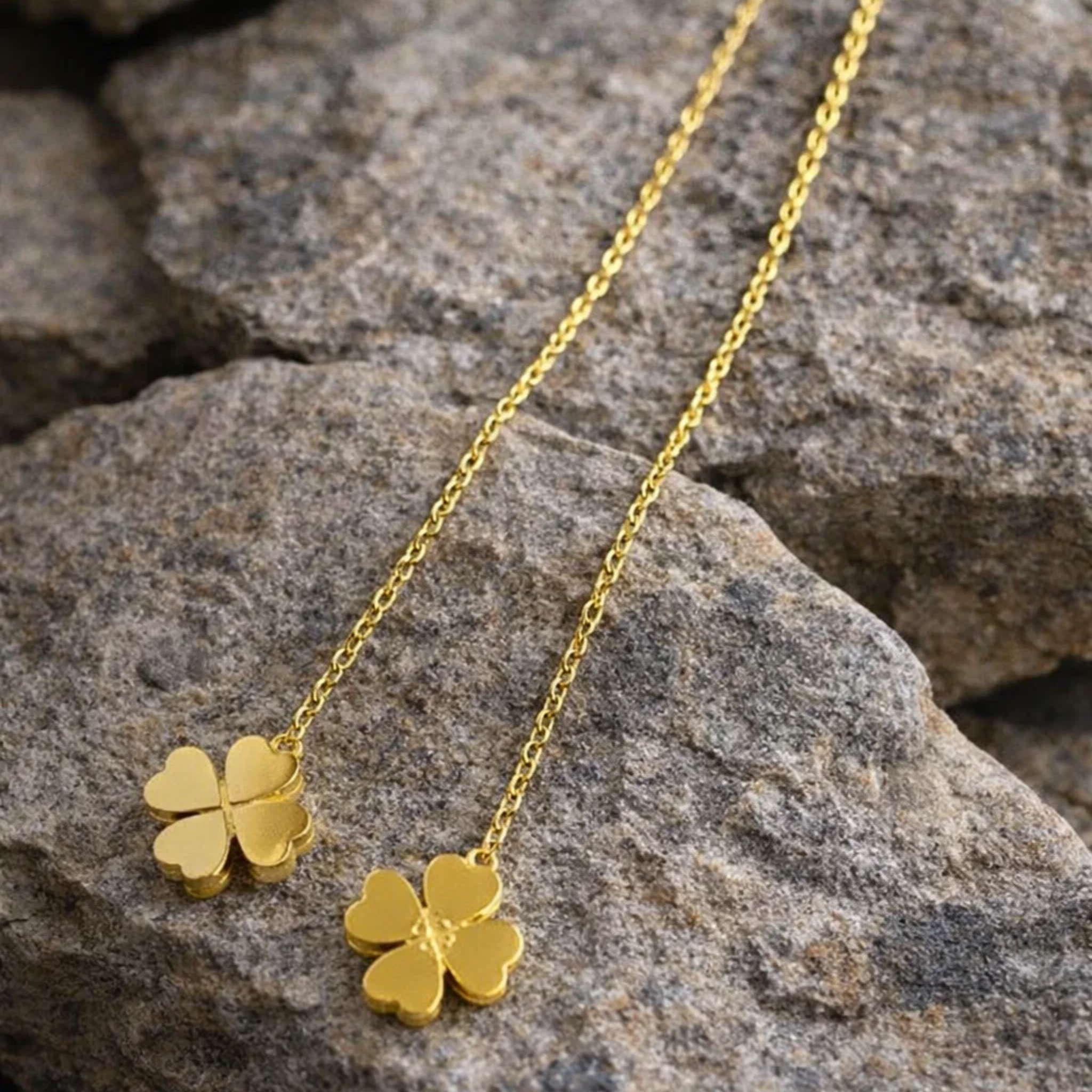 Gold four-leaf clover earrings on a stone surface
