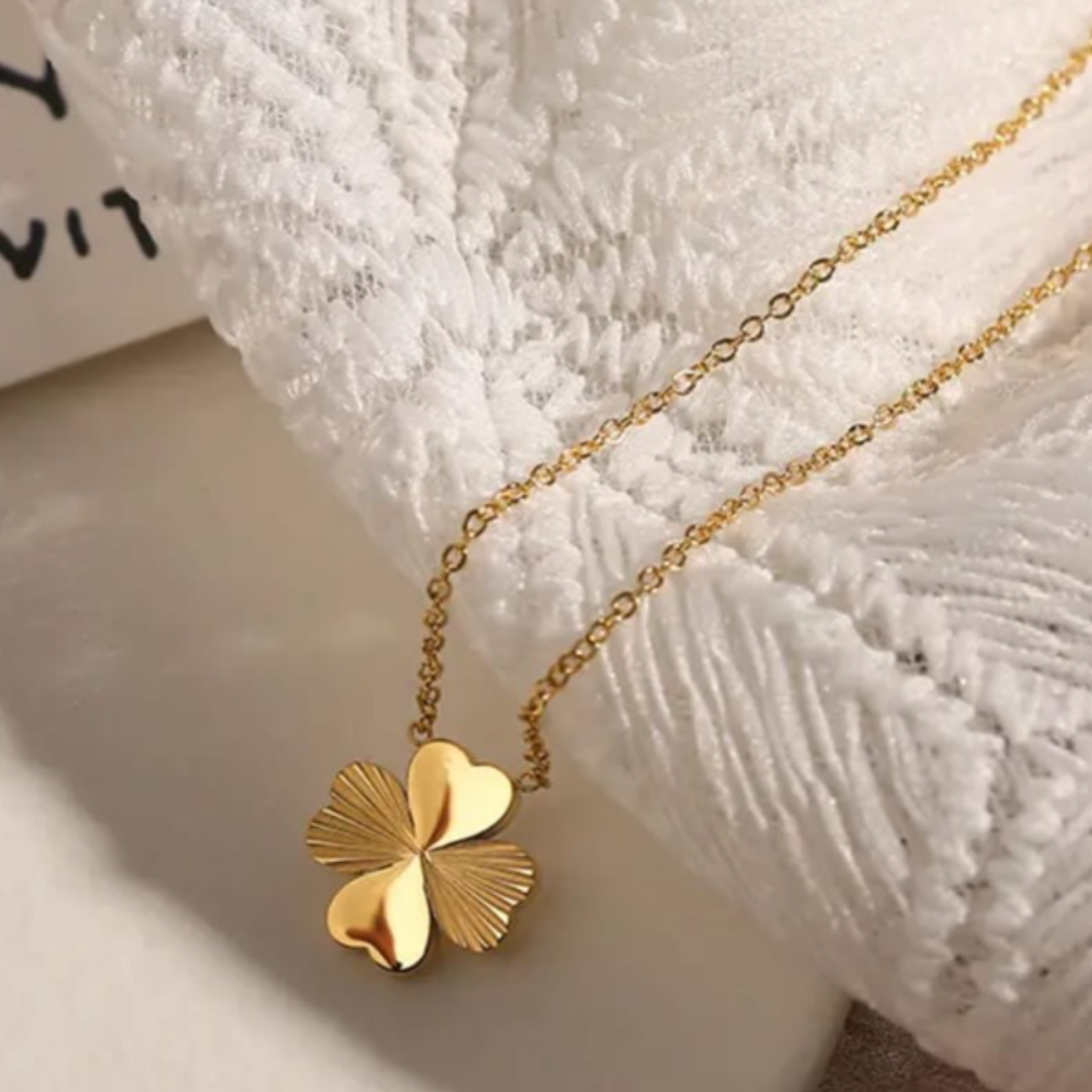 Gold four-leaf clover necklace on a textured white surface