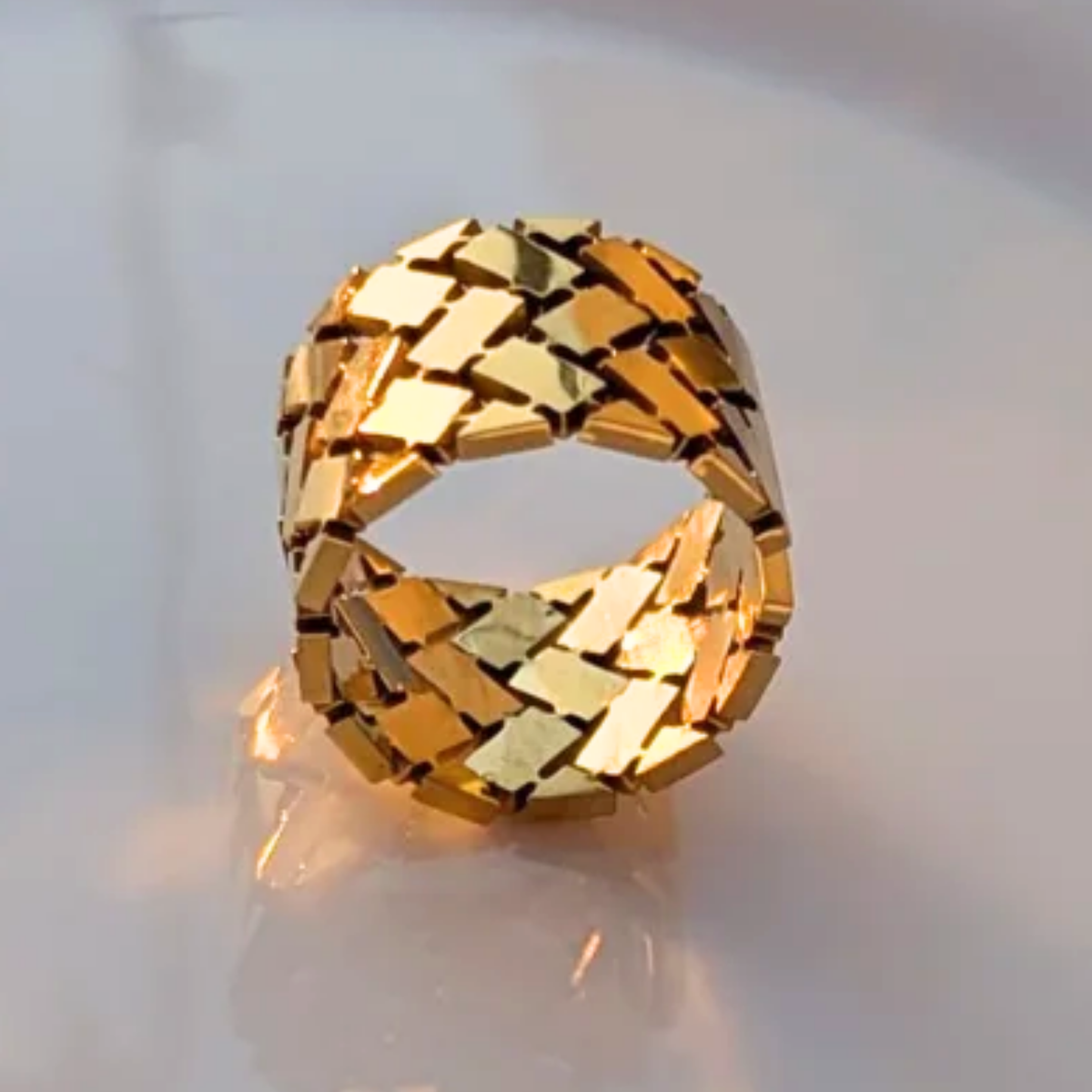 A wide band ring with a geometric, interlocking metallic pattern 