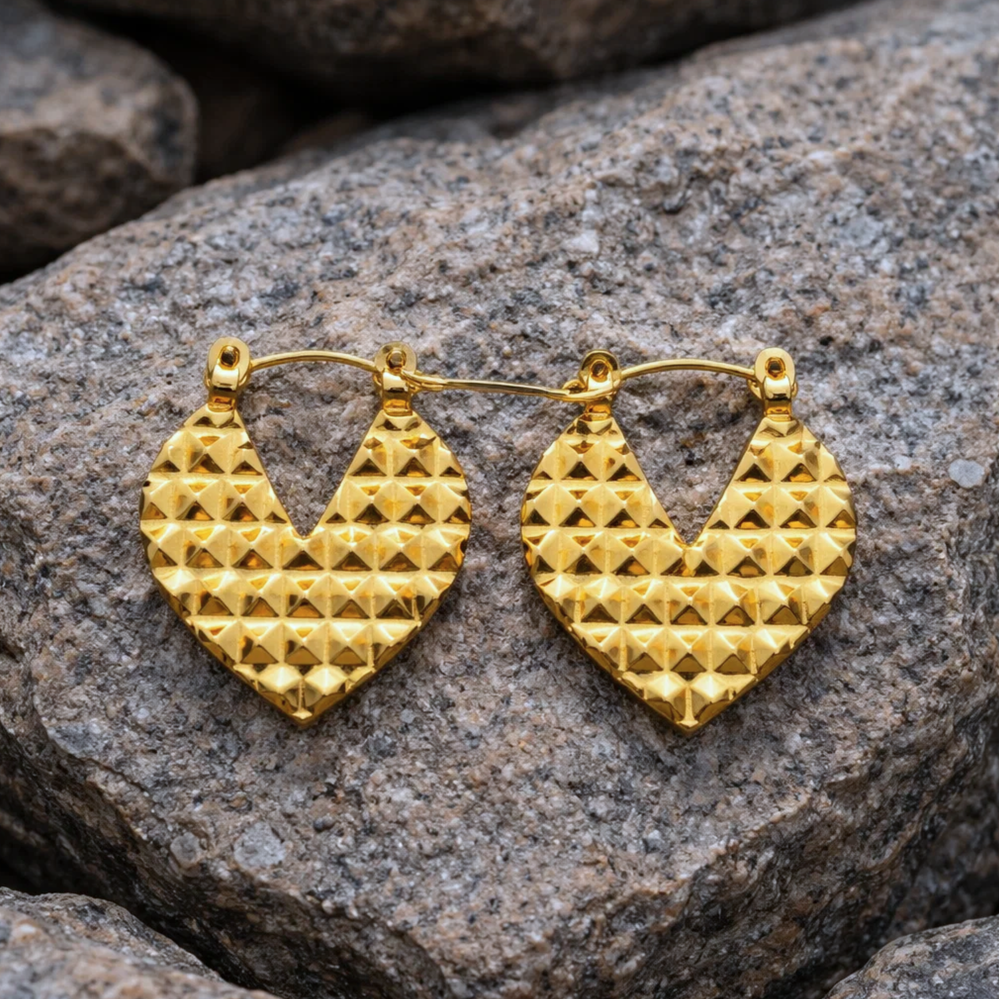 Gold heart-shaped earrings on a stone surface