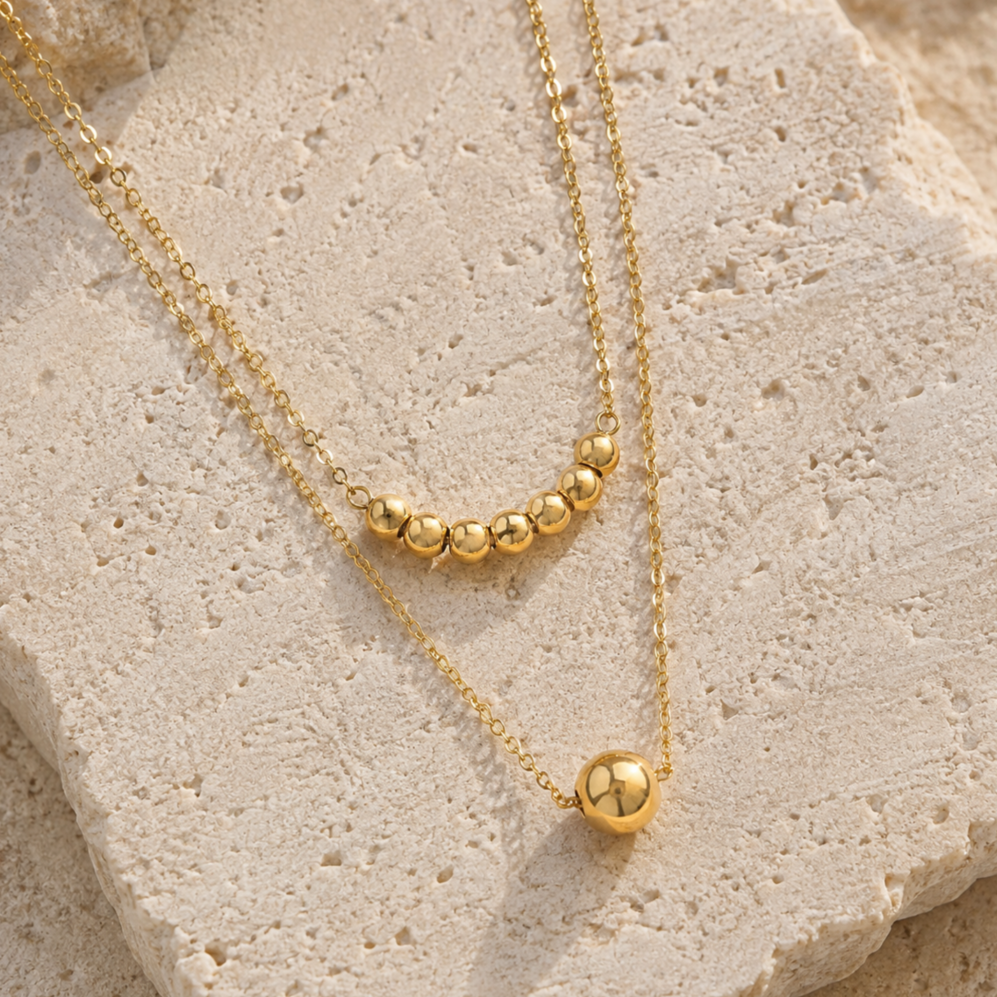Two chained gold bead necklace on a stone surface