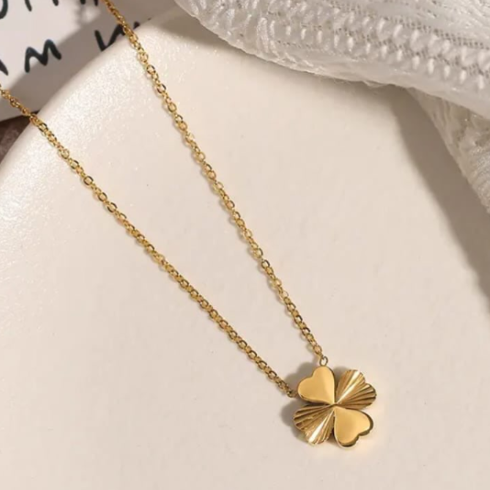 Gold four-leaf clover necklace on a ceramic plate