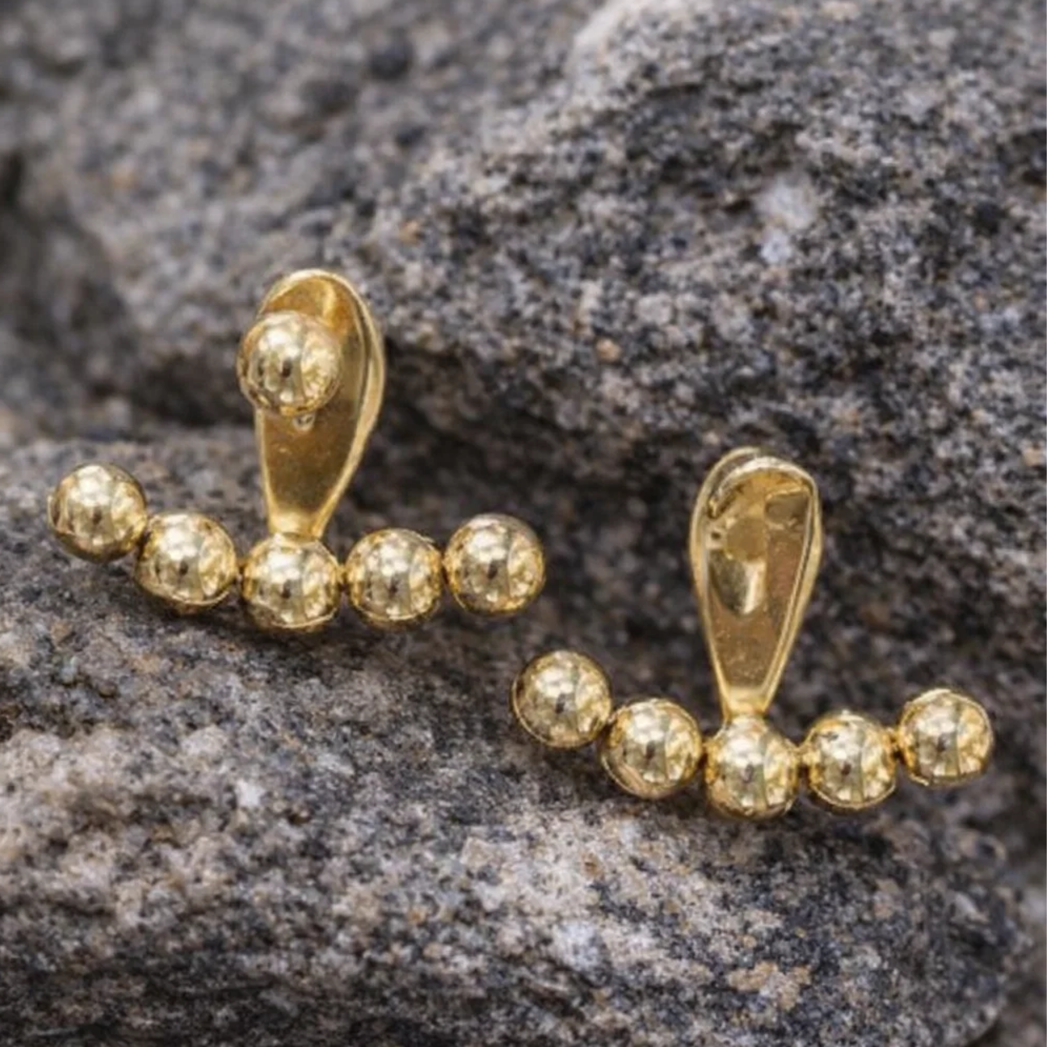 Gold beaded earring on a textured stone surface