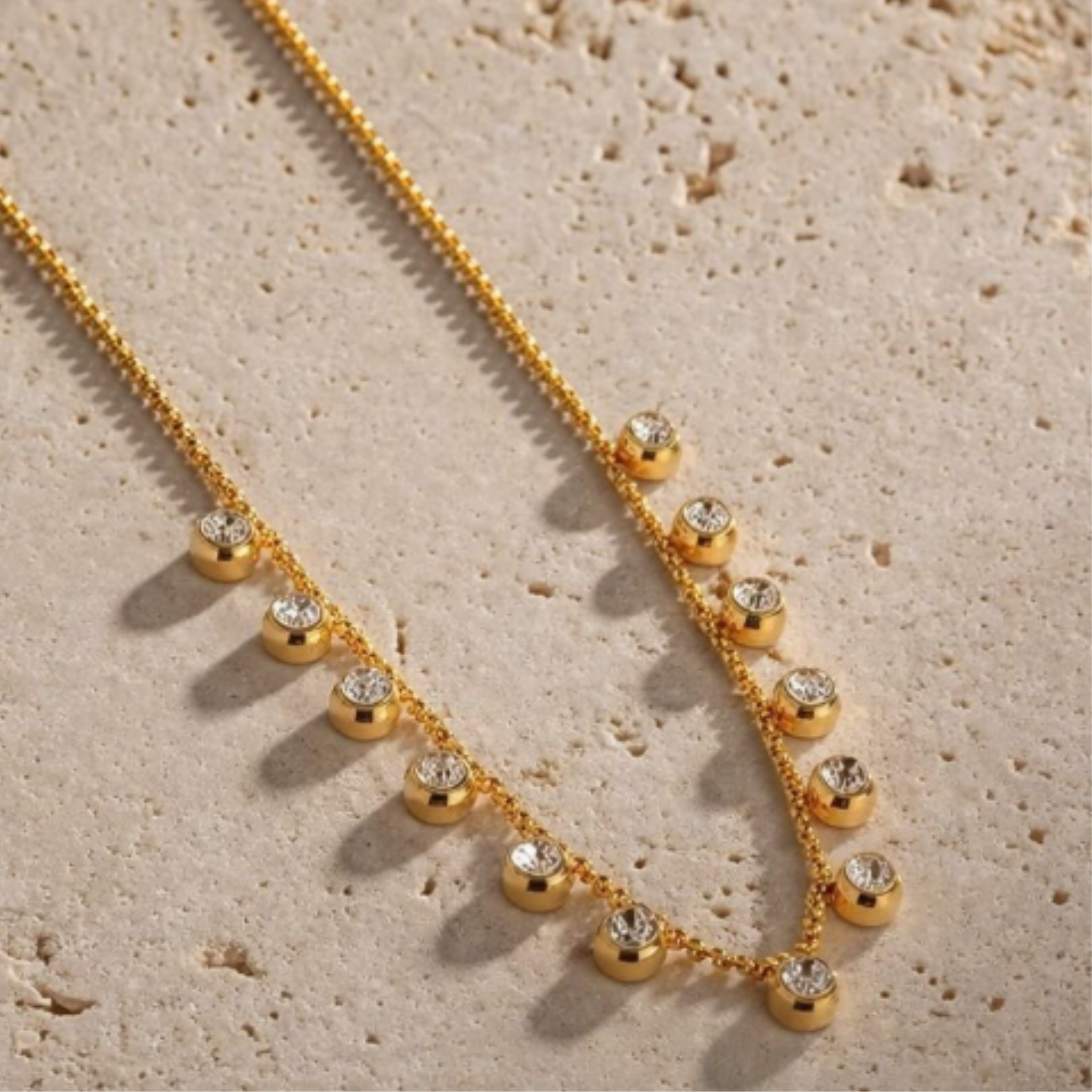 Gold necklace with small beads and crystals on a textured beige surface
