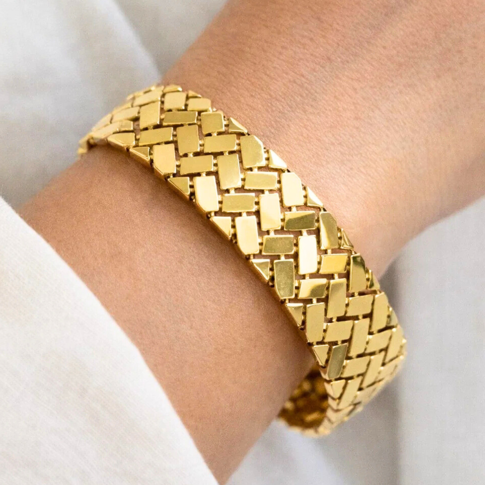 Gold bracelet on a wrist with a neutral background