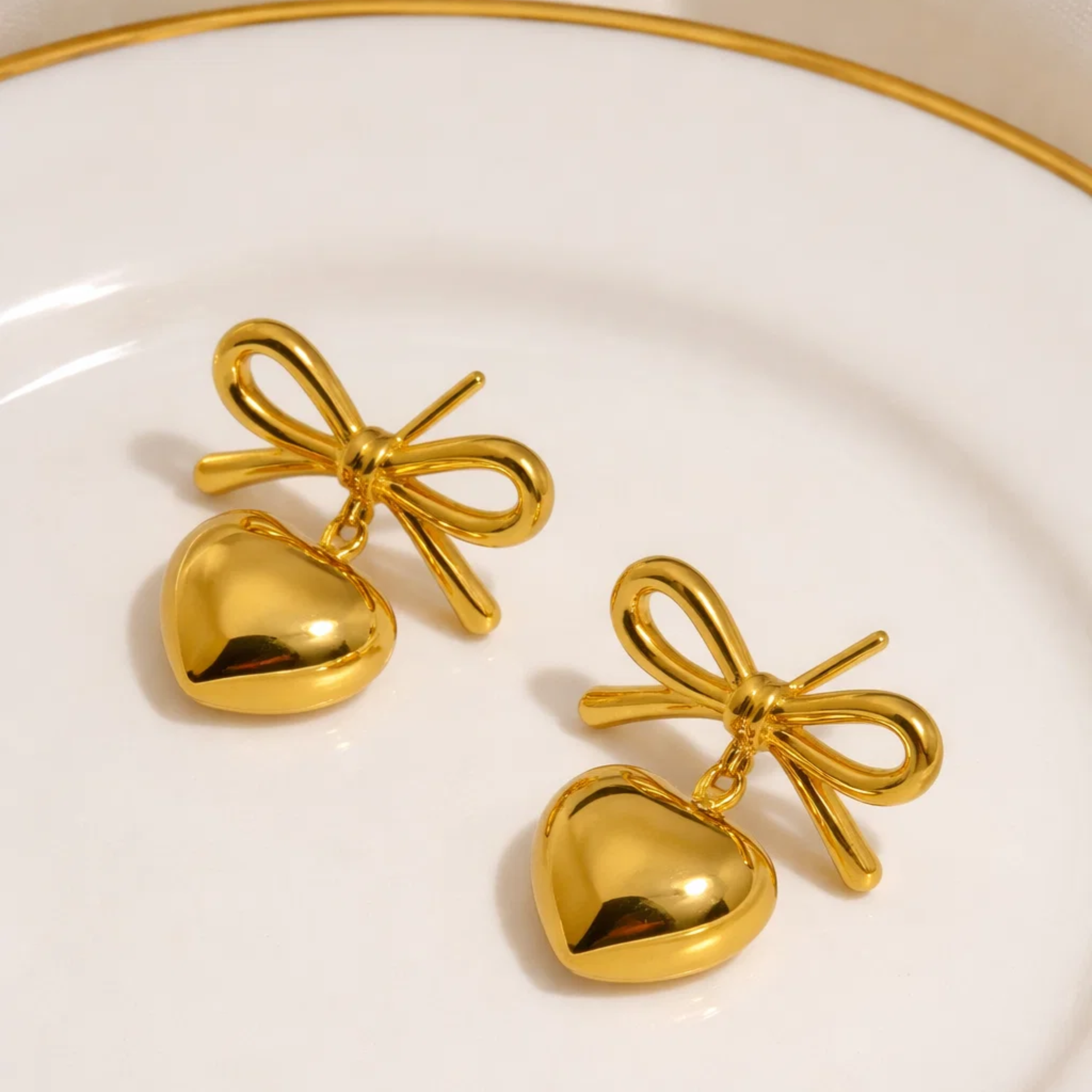 Gold heart-shaped earrings with bow details on a white plate.