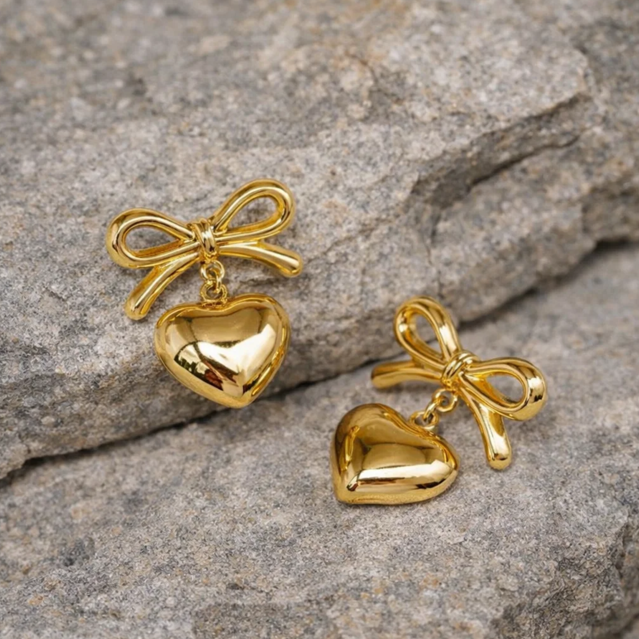 Gold heart and bow earrings on a stone surface