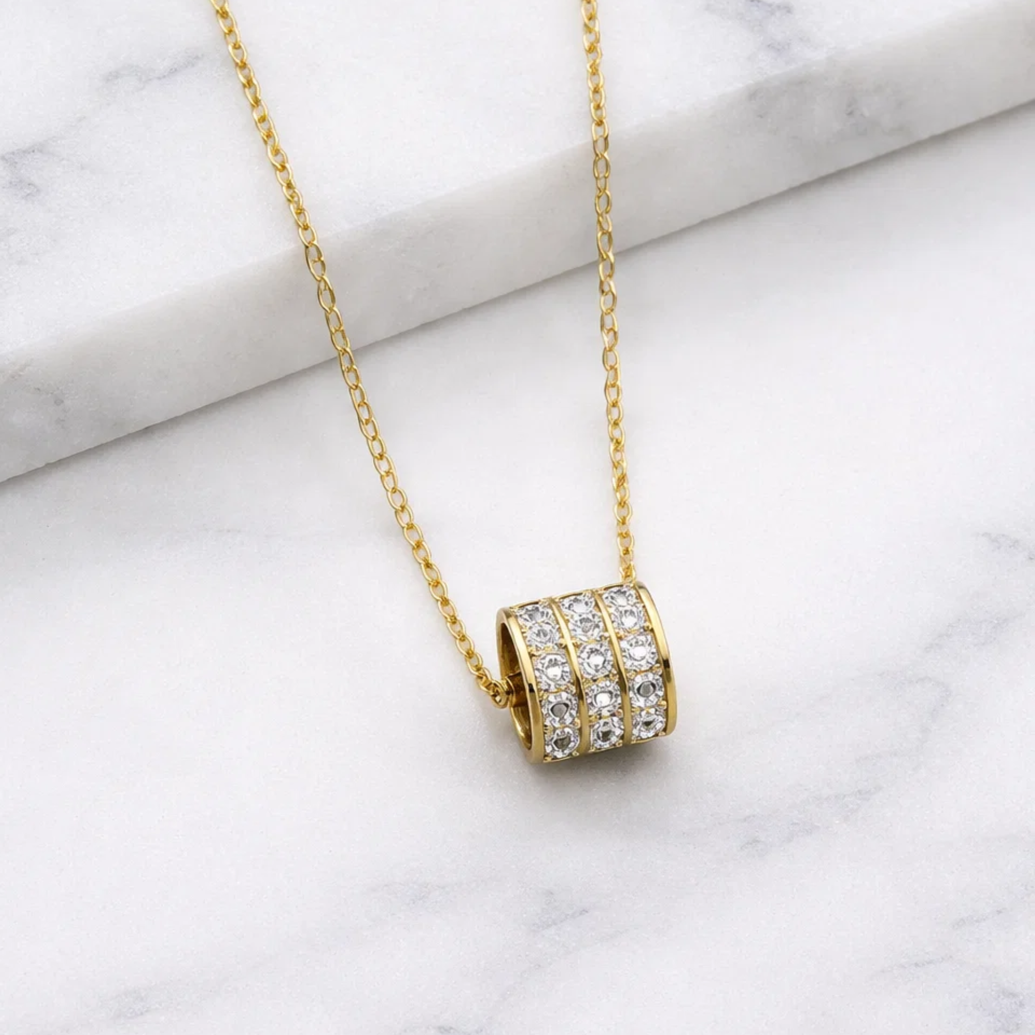 Gold necklace with a cylindrical pendant on a marble surface