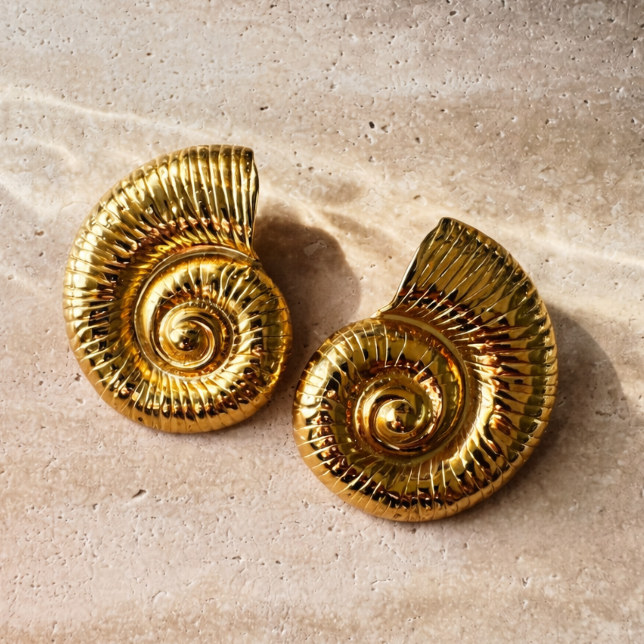 Pair of gold spiral earrings on a beige surface