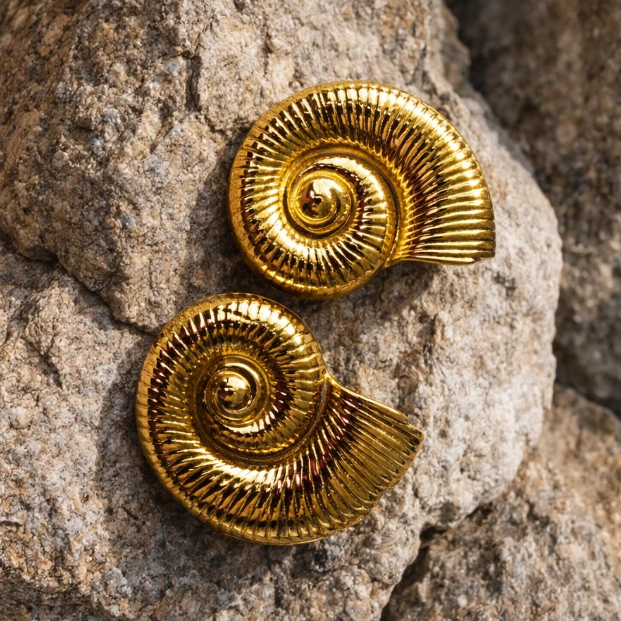Gold spiral earrings on a textured stone surface