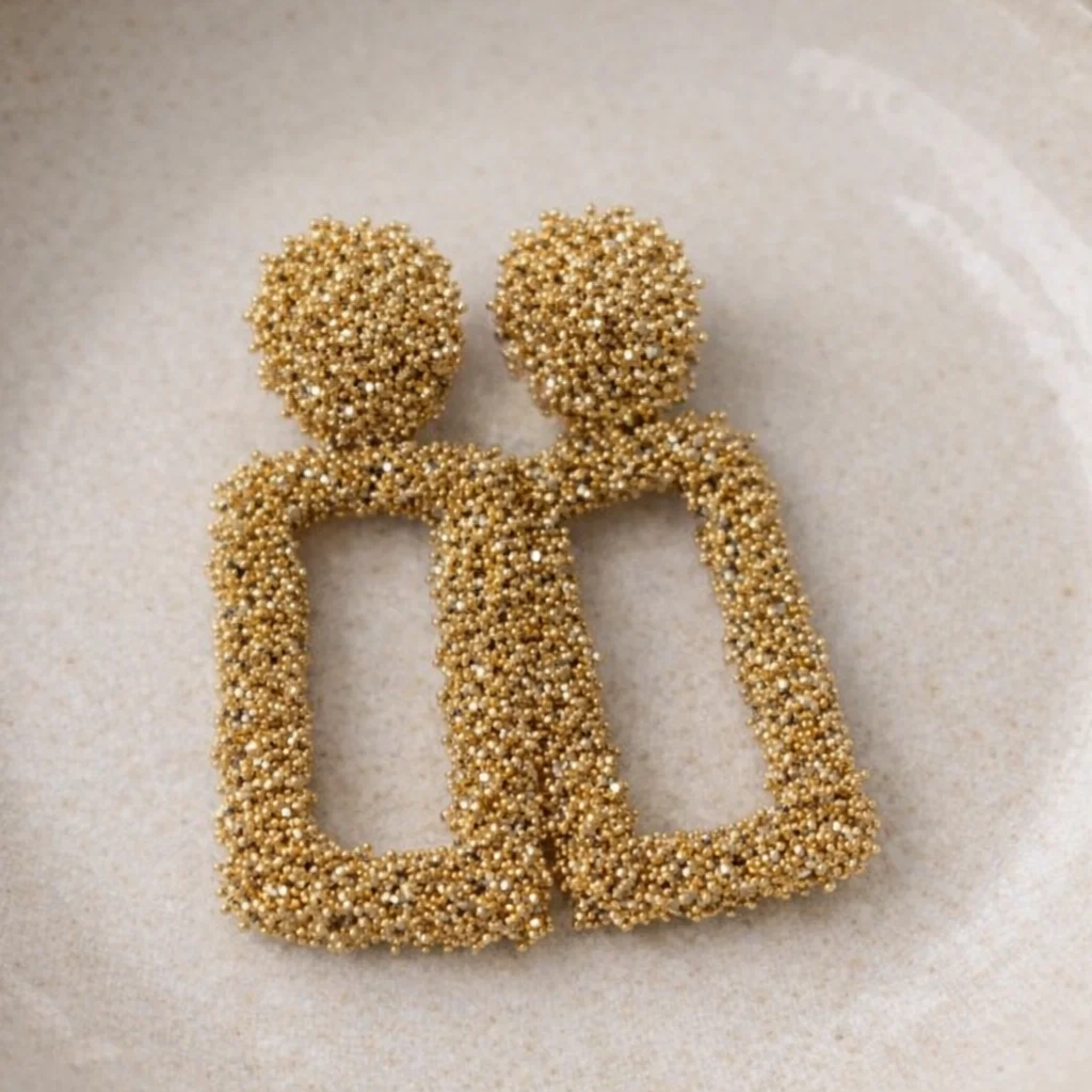 Gold stainless earrings on a ceramic plate