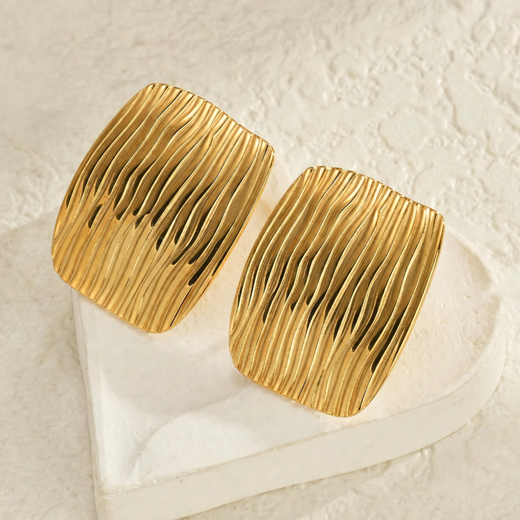 Gold earrings on a textured beige surface
