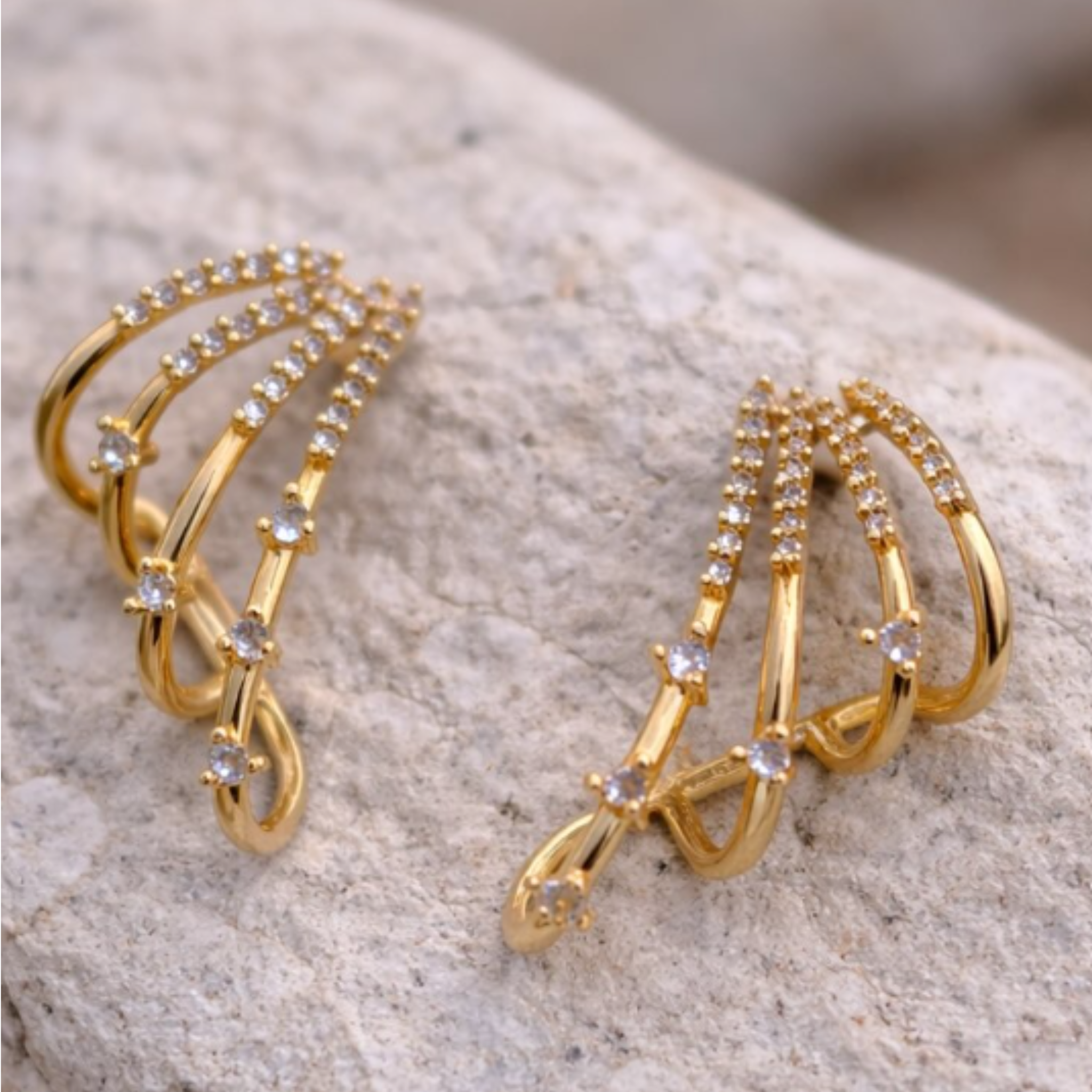 Gold ear cuffs with gemstones on a textured stone surface