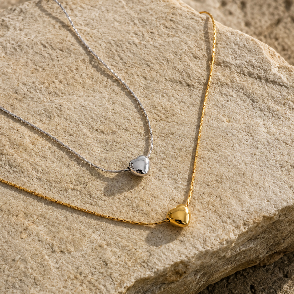 Two minimalistic silver and gold heart pendants on a rock surface