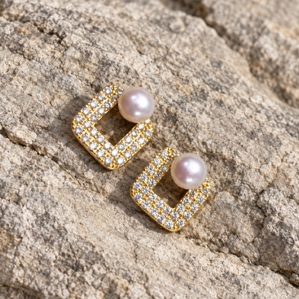 A pair of gold square stud earrings with a central round pearl 