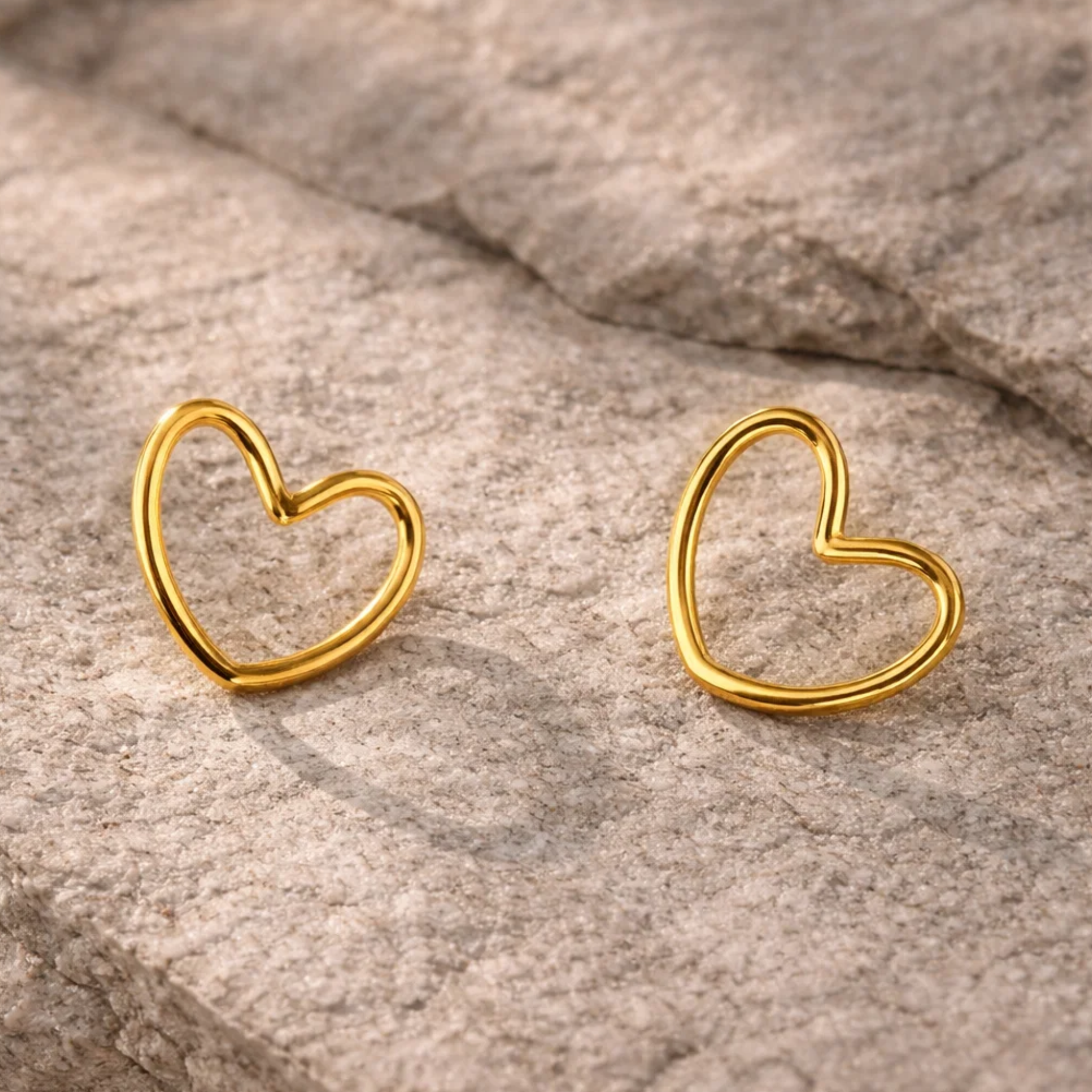 Gold heart-shaped earrings on a textured stone surface