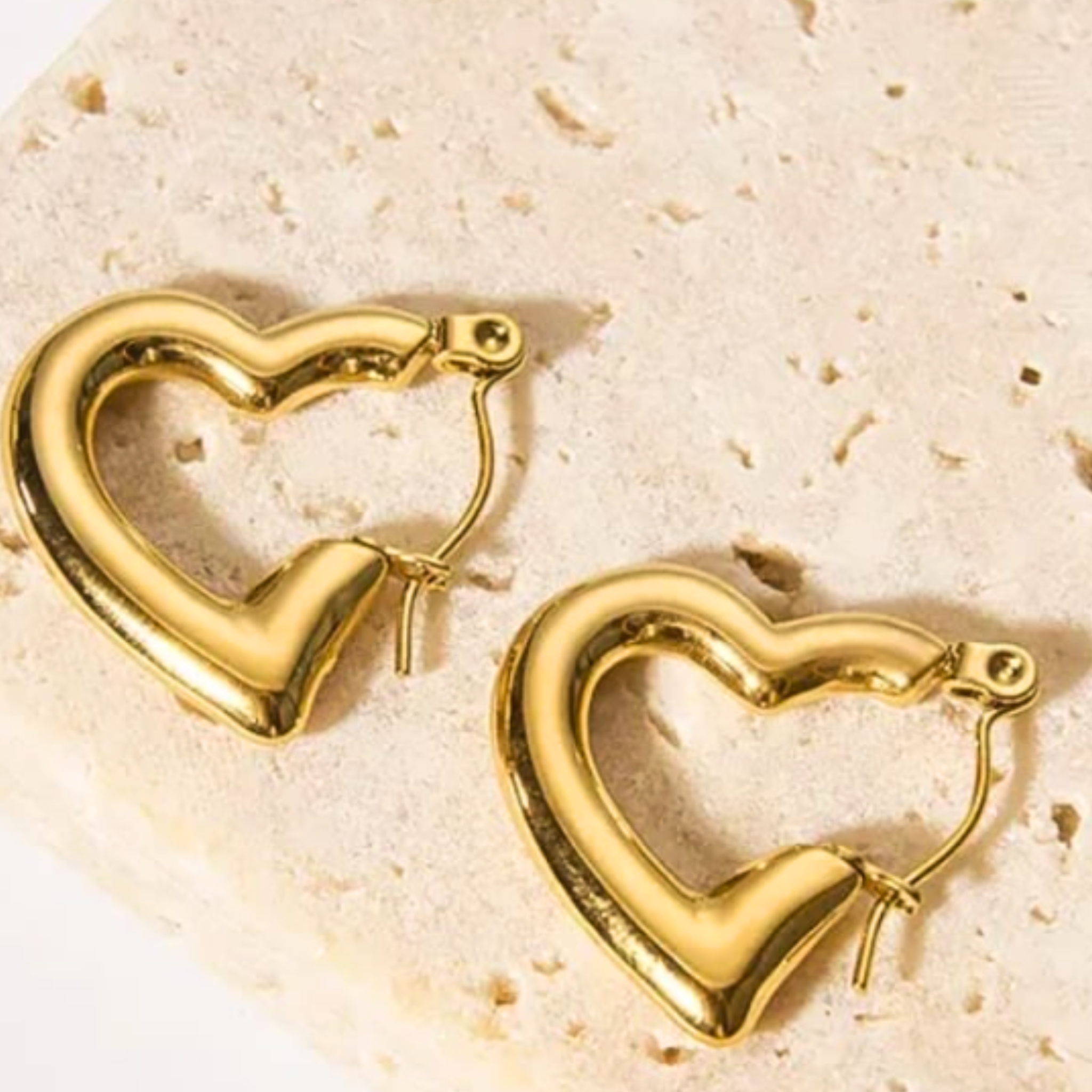 Gold heart-shaped hoop earrings on a beige stone surface