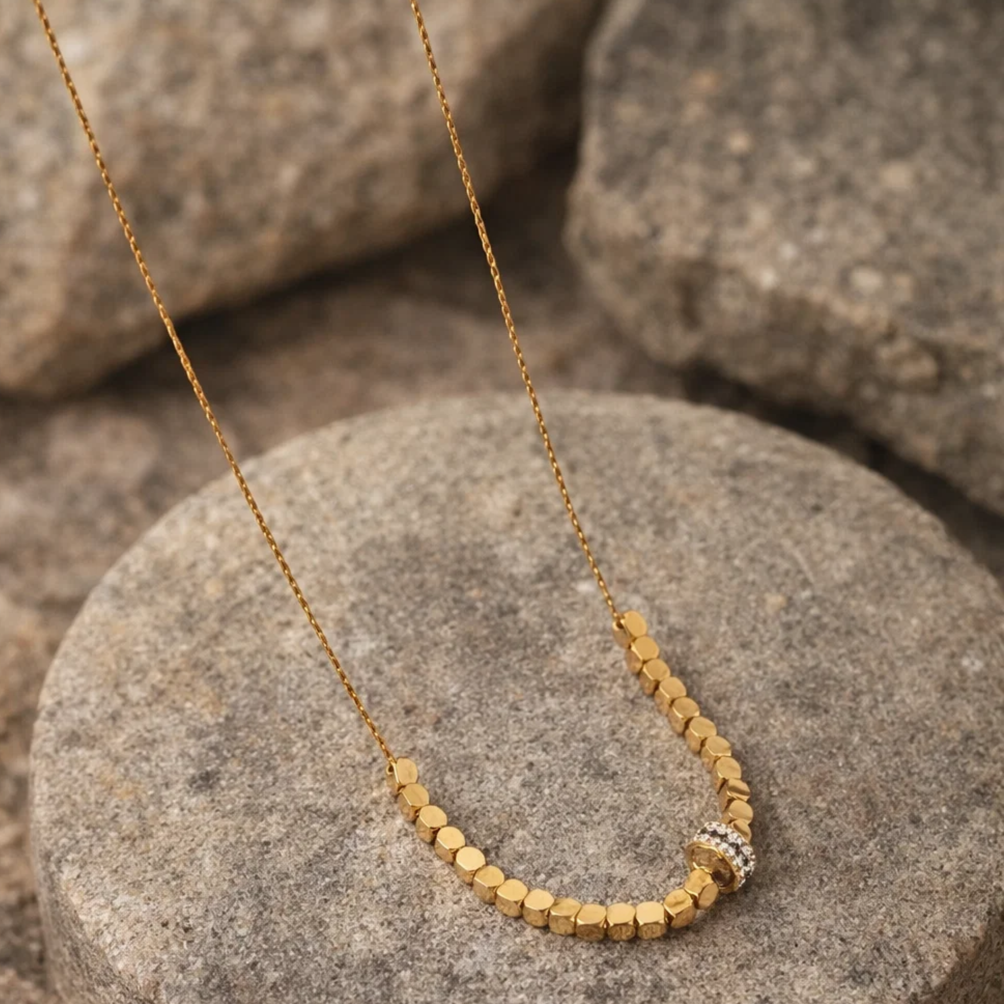 Gold necklace with hexagonal beads on a stone surface