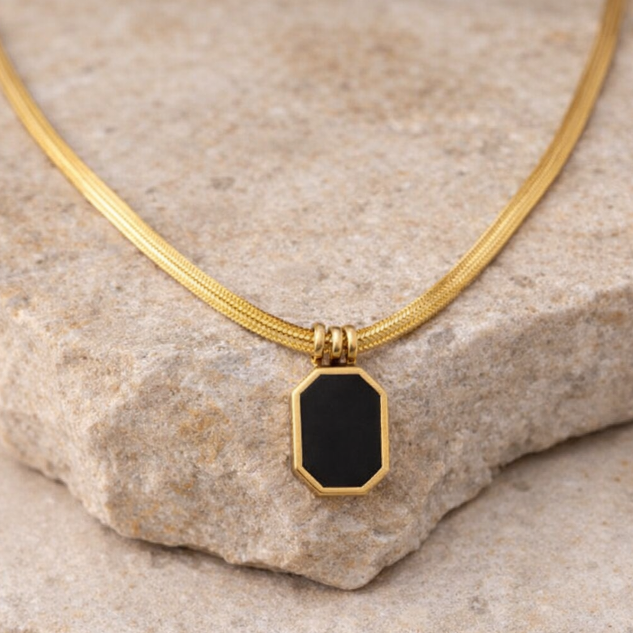 Gold necklace with a black pendant on a stone surface