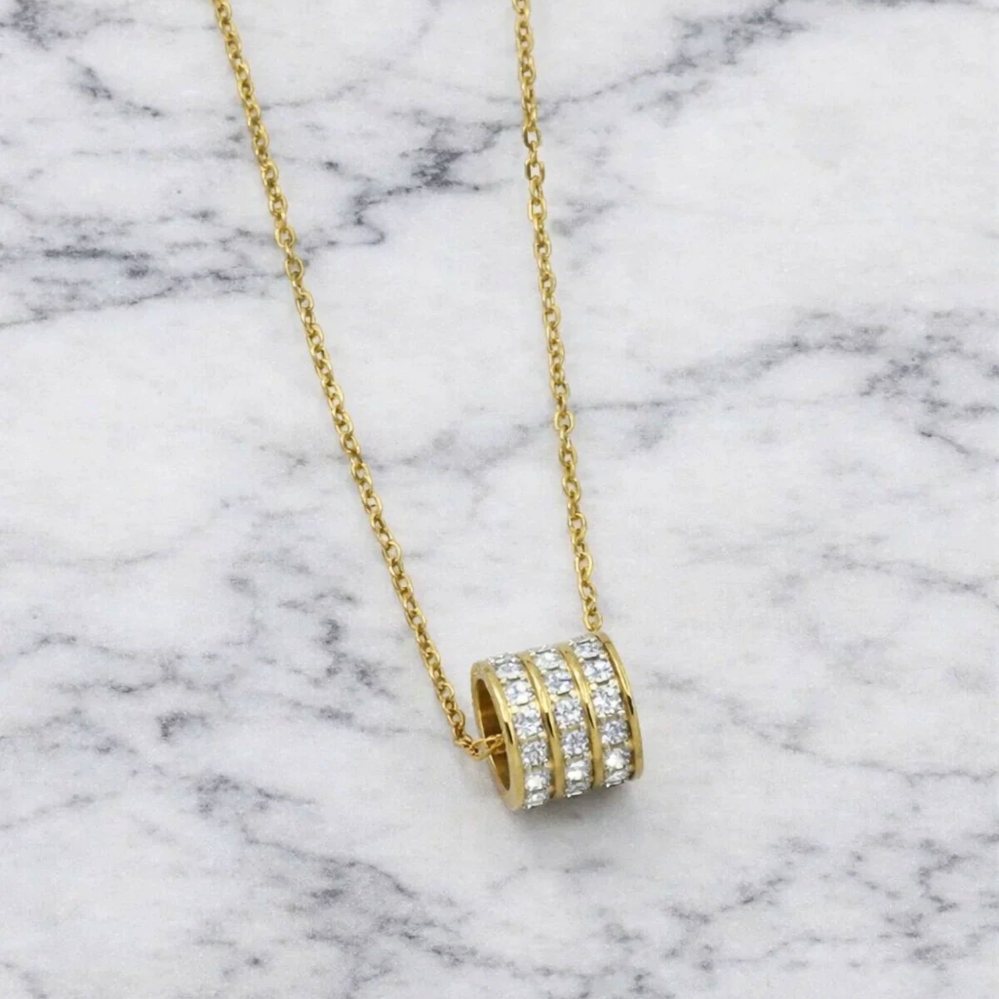 Gold necklace with a diamond pendant on a marble background