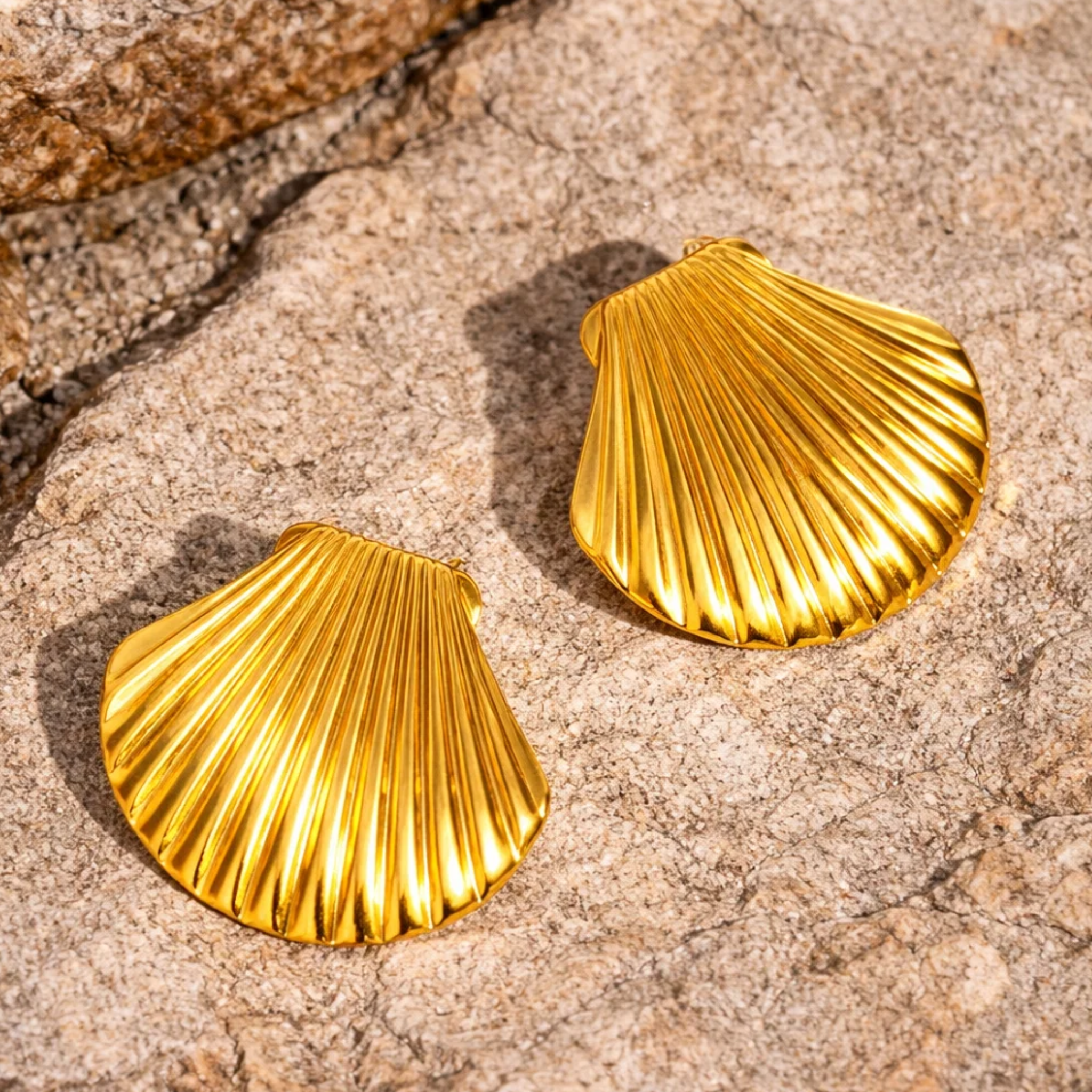 Gold shell-shaped earrings on a stone surface