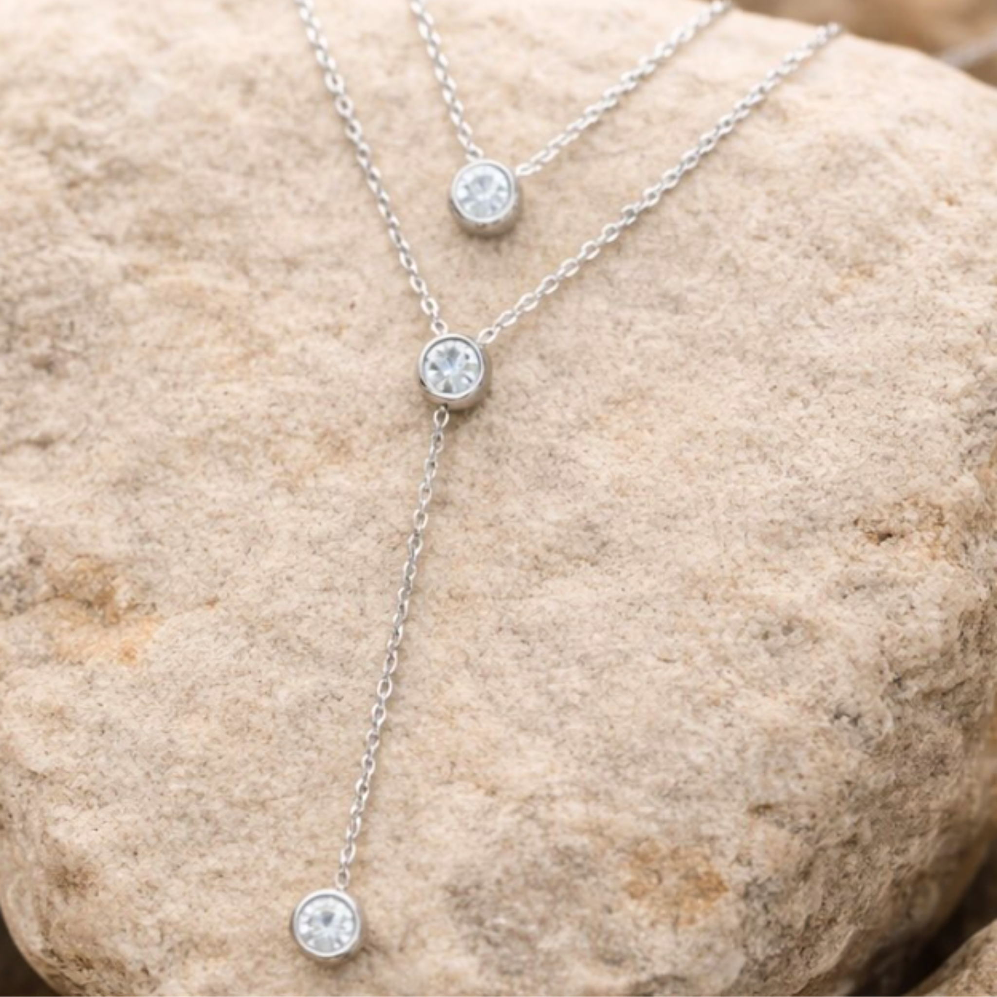 Silver necklace with three round pendants on a stone surface