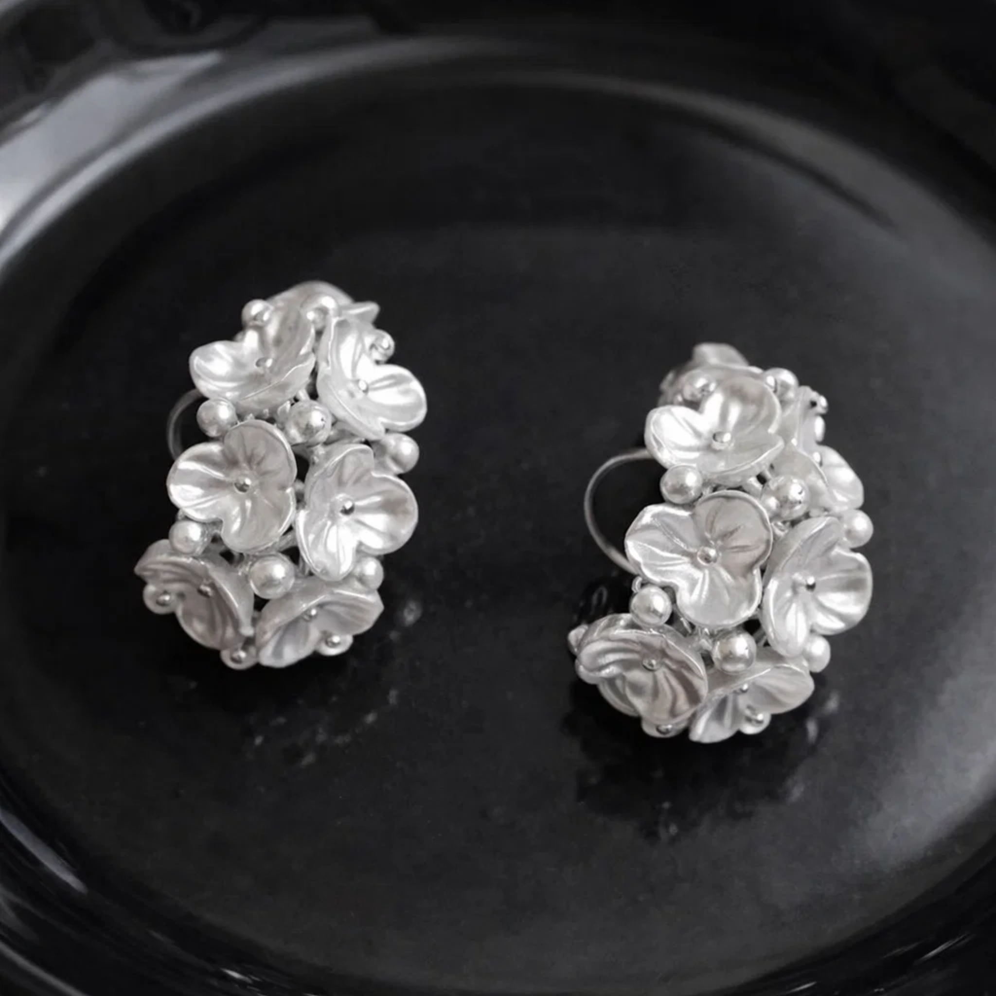 Pair of silver floral earrings on a black plate