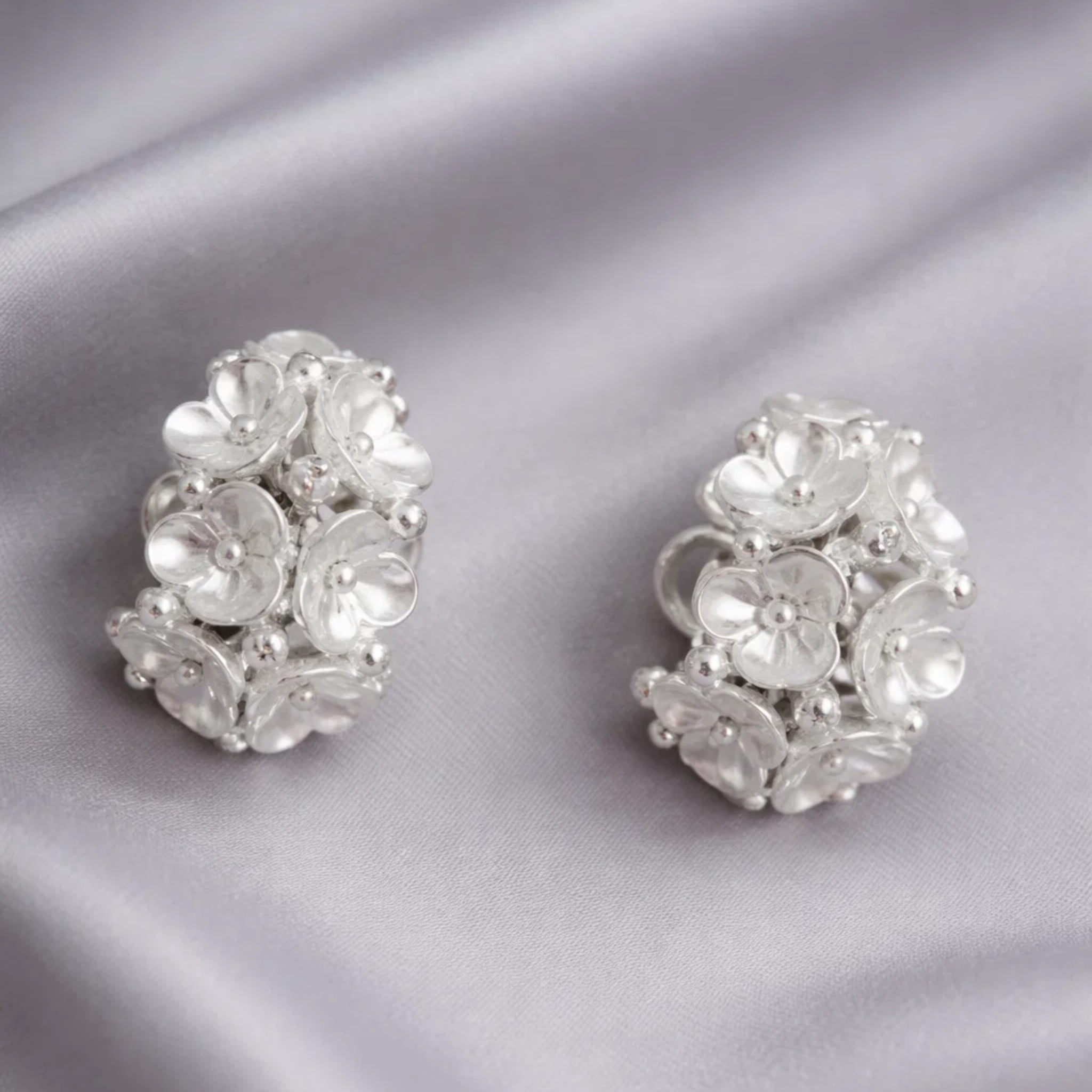 Pair of silver floral earrings on a gray fabric 