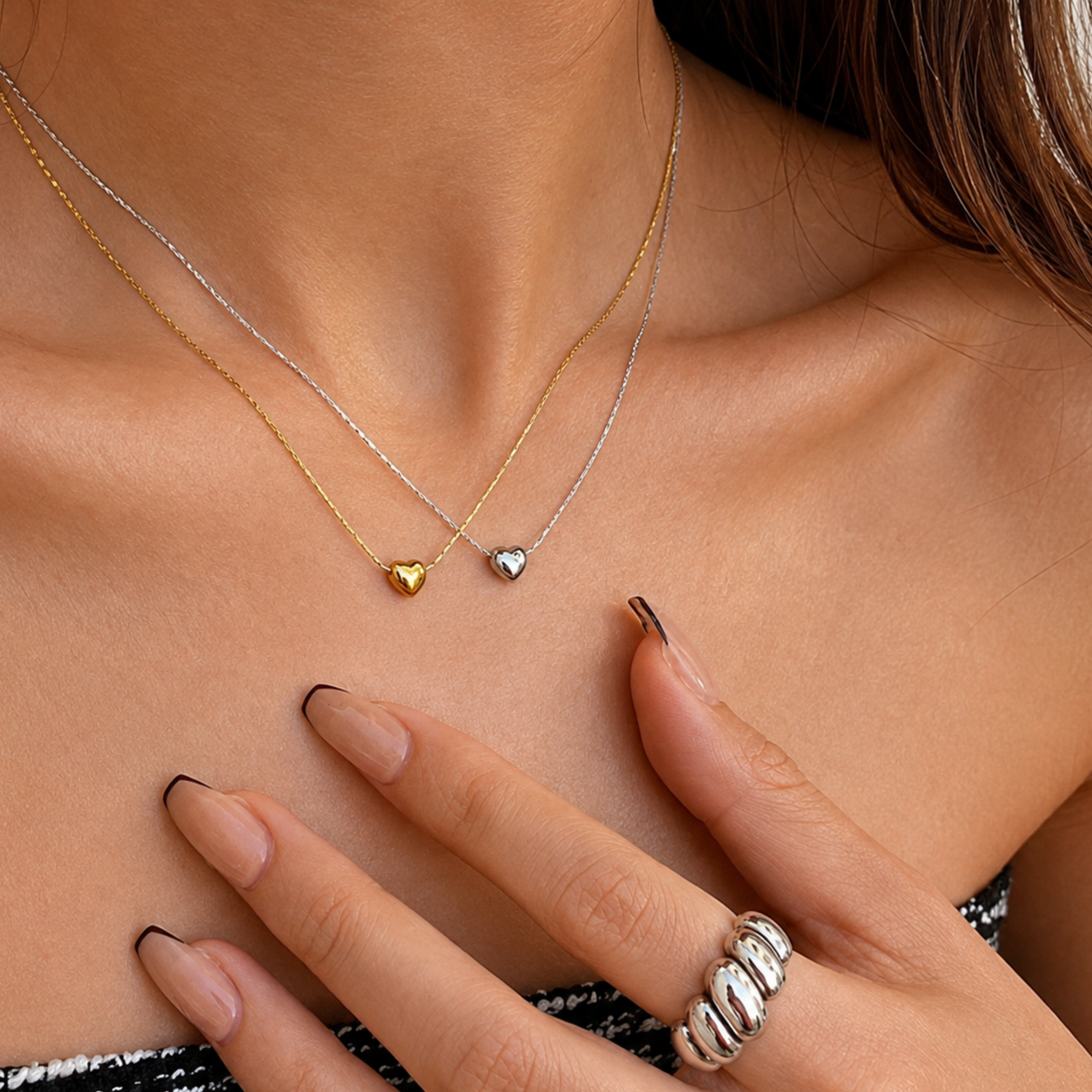 A woman is wearing silver and gold heart-shaped necklace together