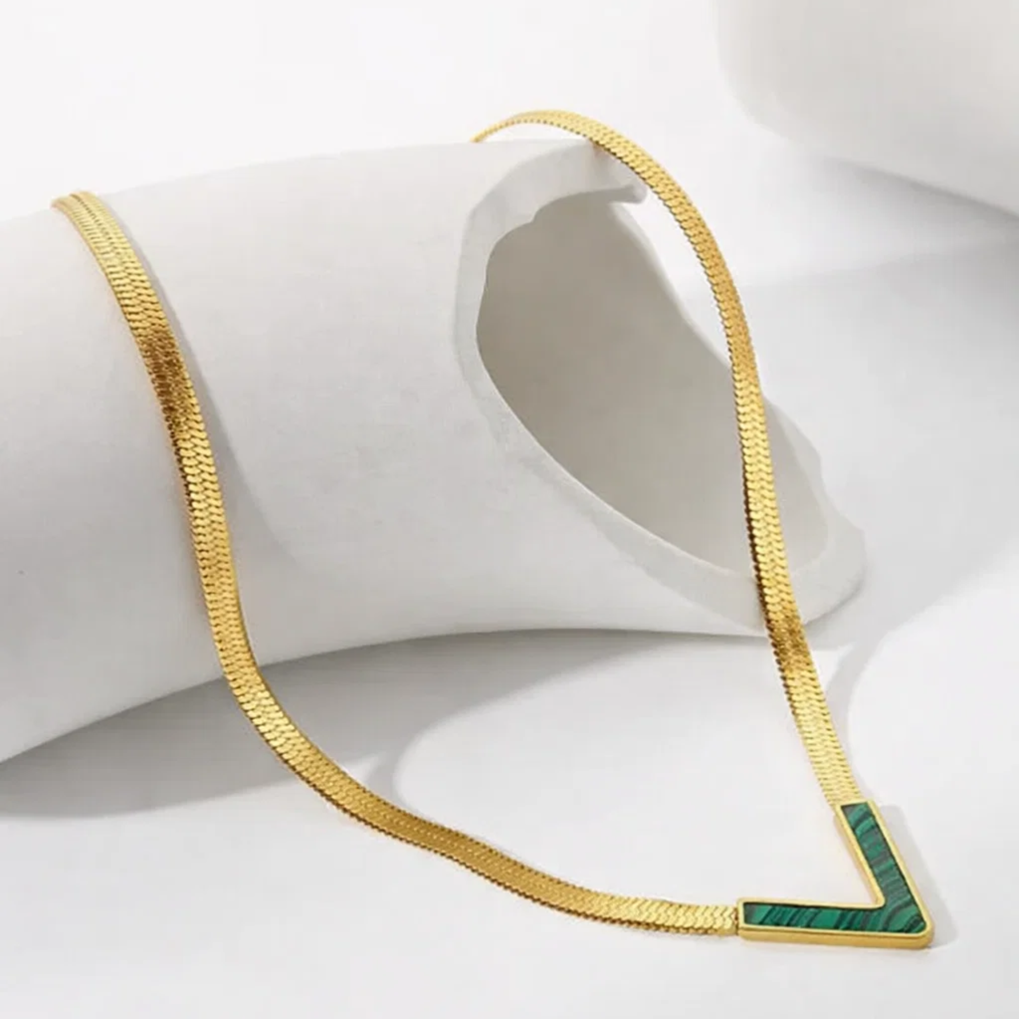 Gold necklace with a green pendant on a white surface