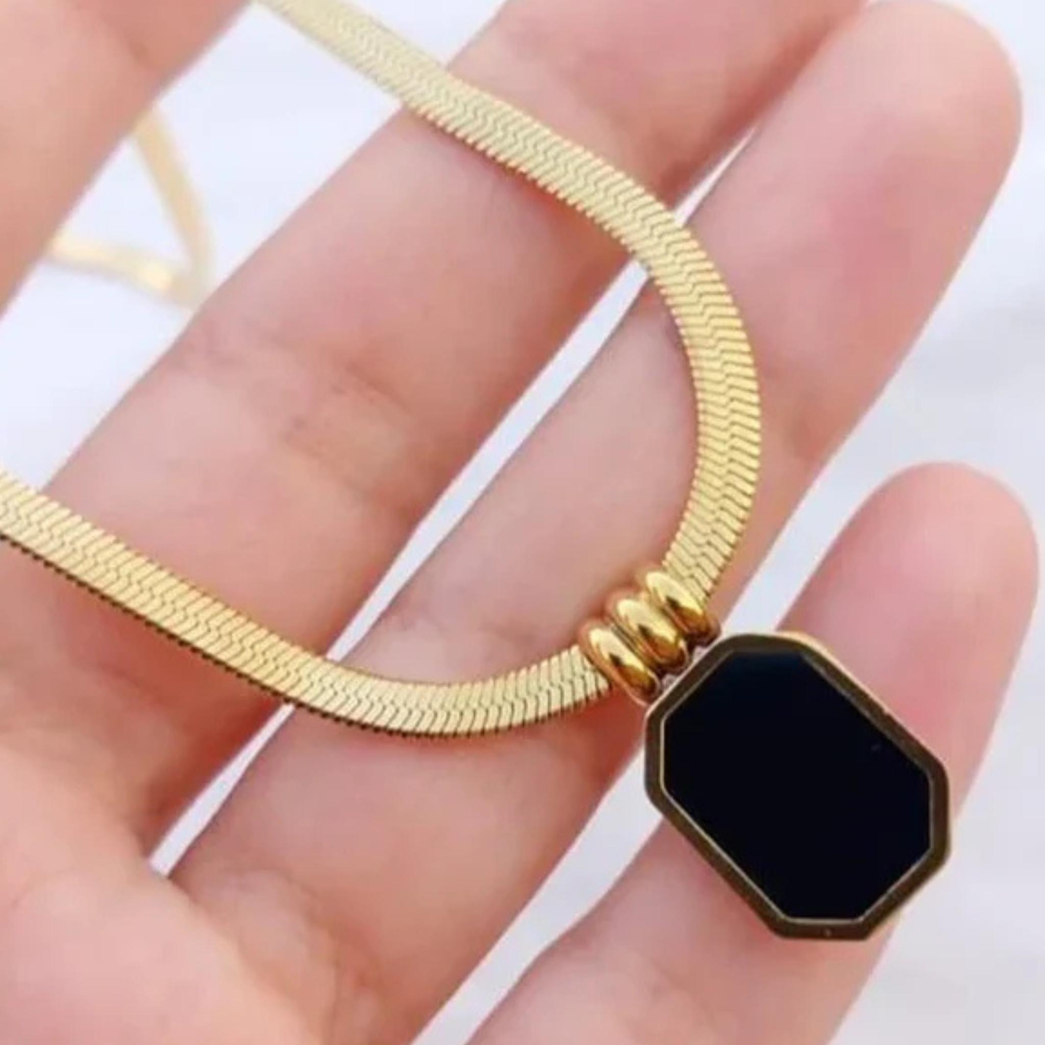 Gold necklace with a black hexagonal pendant held in a hand 