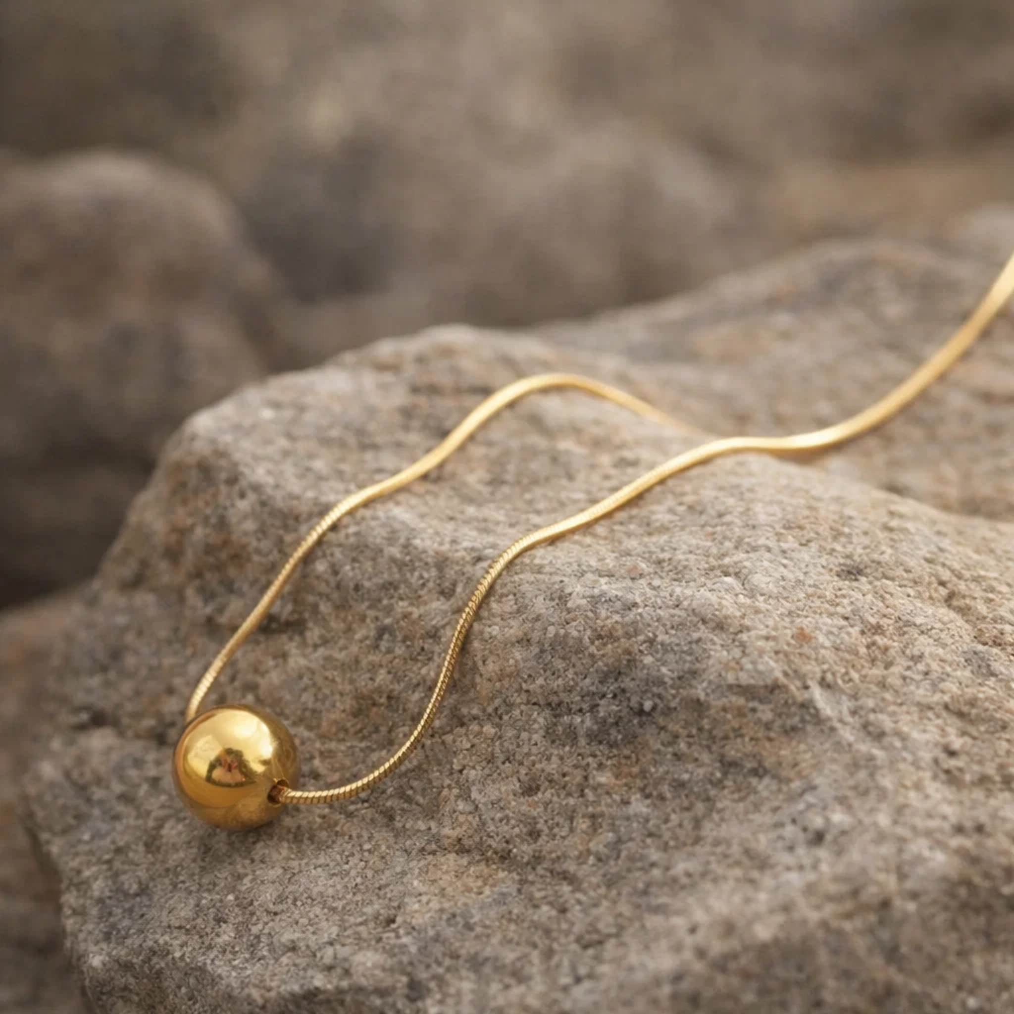 Gold necklace with a spherical pendant on a stone surface