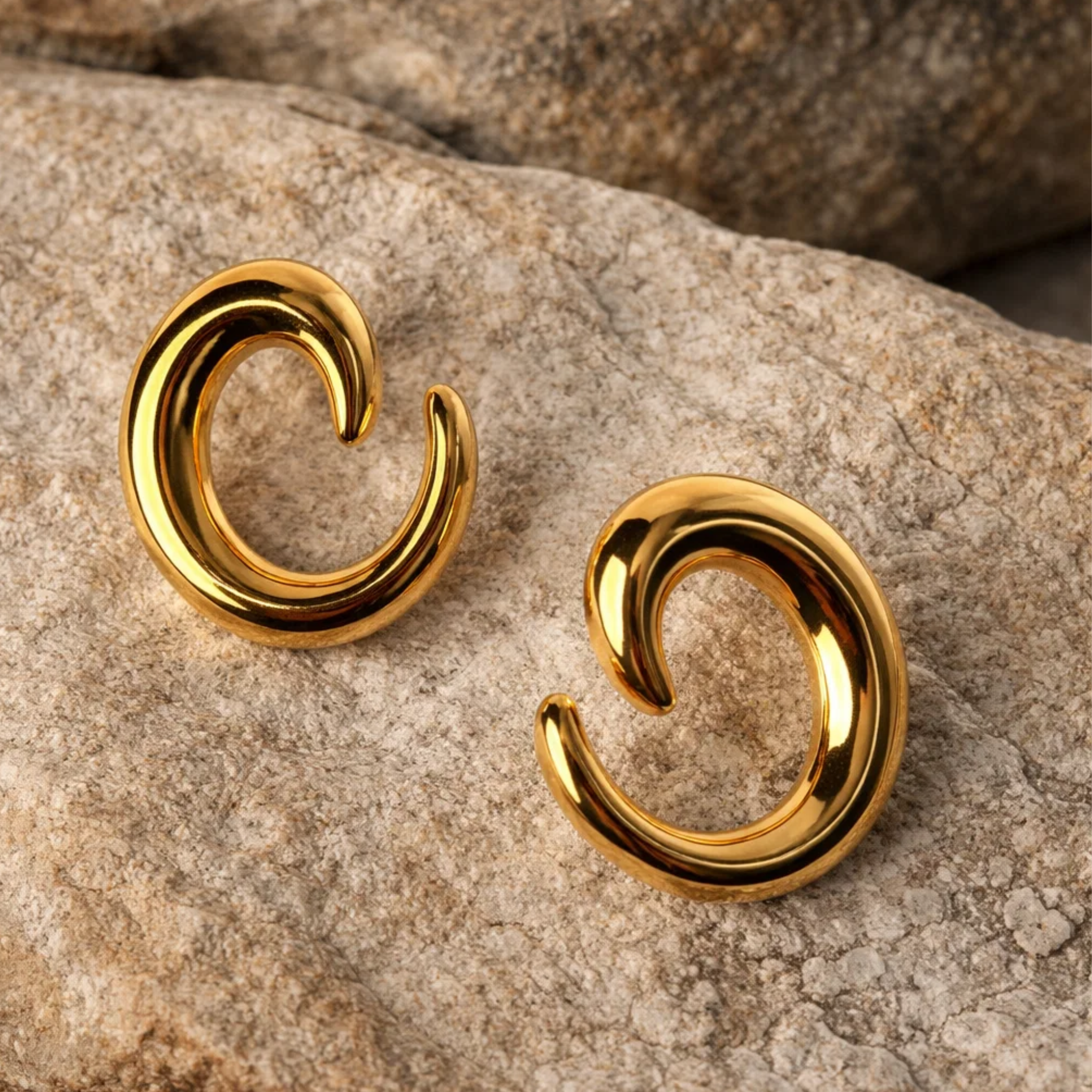 Gold spiral earrings on a stone surface
