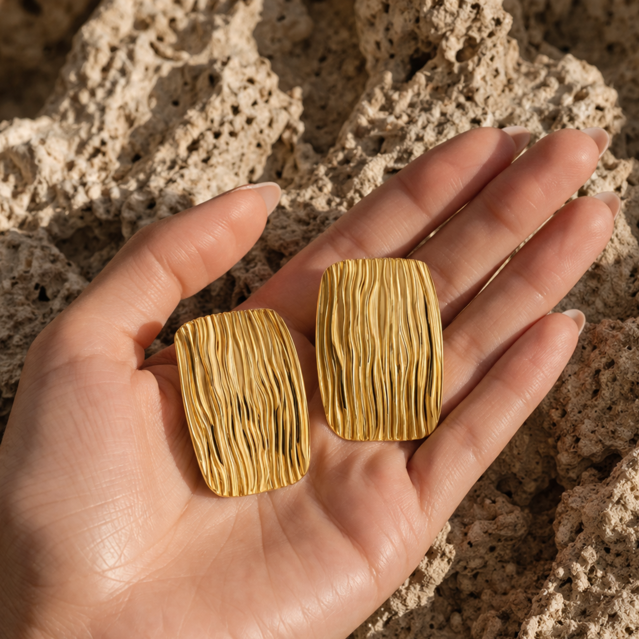 Gold textured square earrings held in a hand 