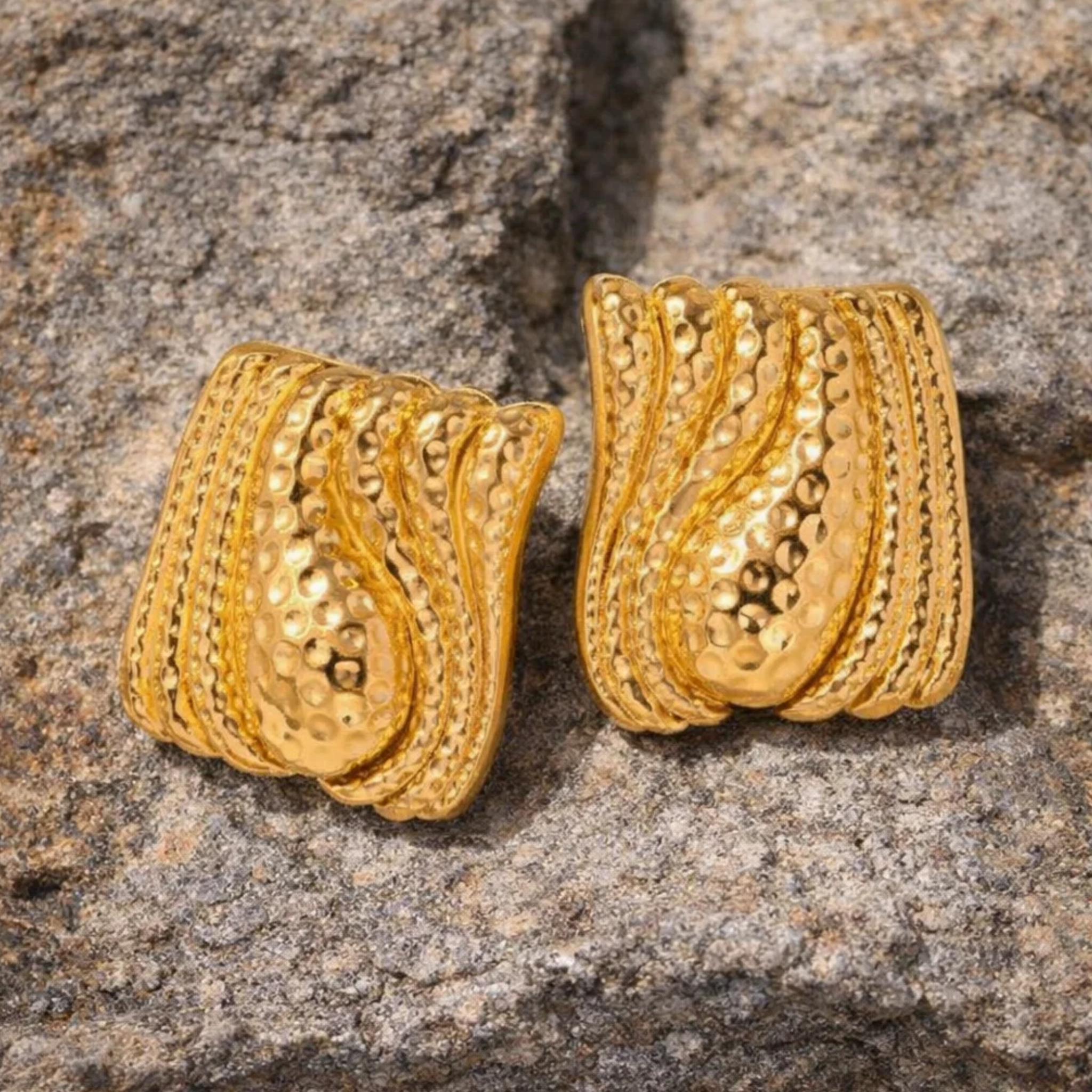Pair of gold earrings on a textured stone surface